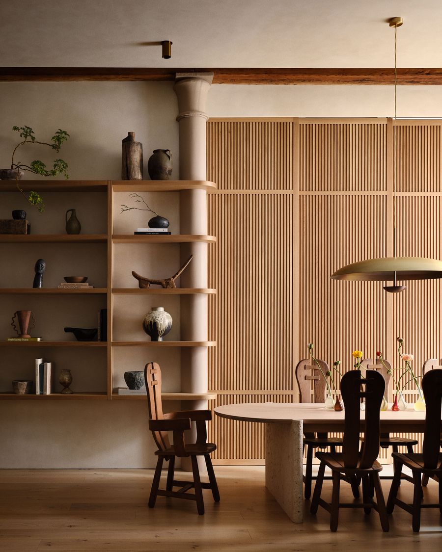 A stylish dining area features wooden chairs, a stone table, and a decorative shelf with artisanal pottery against a textured wall. A stylish dining area features wooden chairs, a stone table, and a decorative shelf with artisanal pottery against a textured wall.