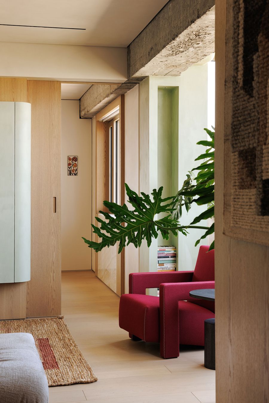 A captivating glimpse into a contemporary interior where thoughtful design maximizes space and light. A biophilic element is prominent with a large, vibrant green plant near a bold red armchair. Beyond, warm wooden walls and a curved pale green panel create a sense of calm and flow, embodying a serene and artful living experience. A captivating glimpse into a contemporary interior where thoughtful design maximizes space and light. A biophilic element is prominent with a large, vibrant green plant near a bold red armchair. Beyond, warm wooden walls and a curved pale green panel create a sense of calm and flow, embodying a serene and artful living experience.