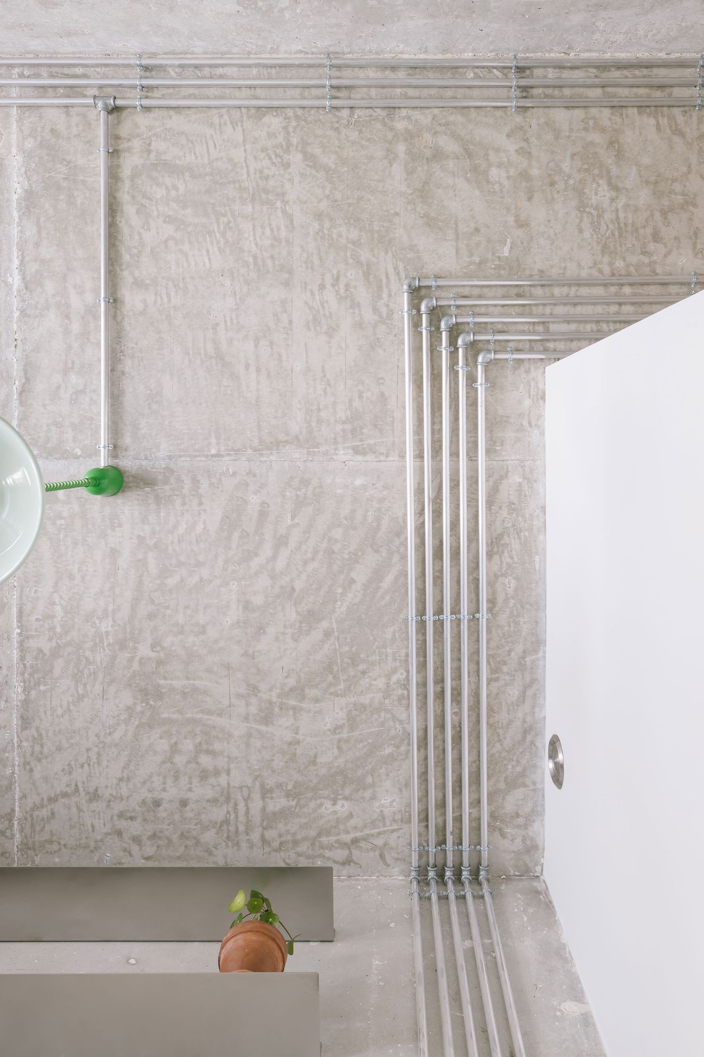 Industrial-style ceiling view featuring grey concrete, metal piping, and a small potted plant on a shelf.