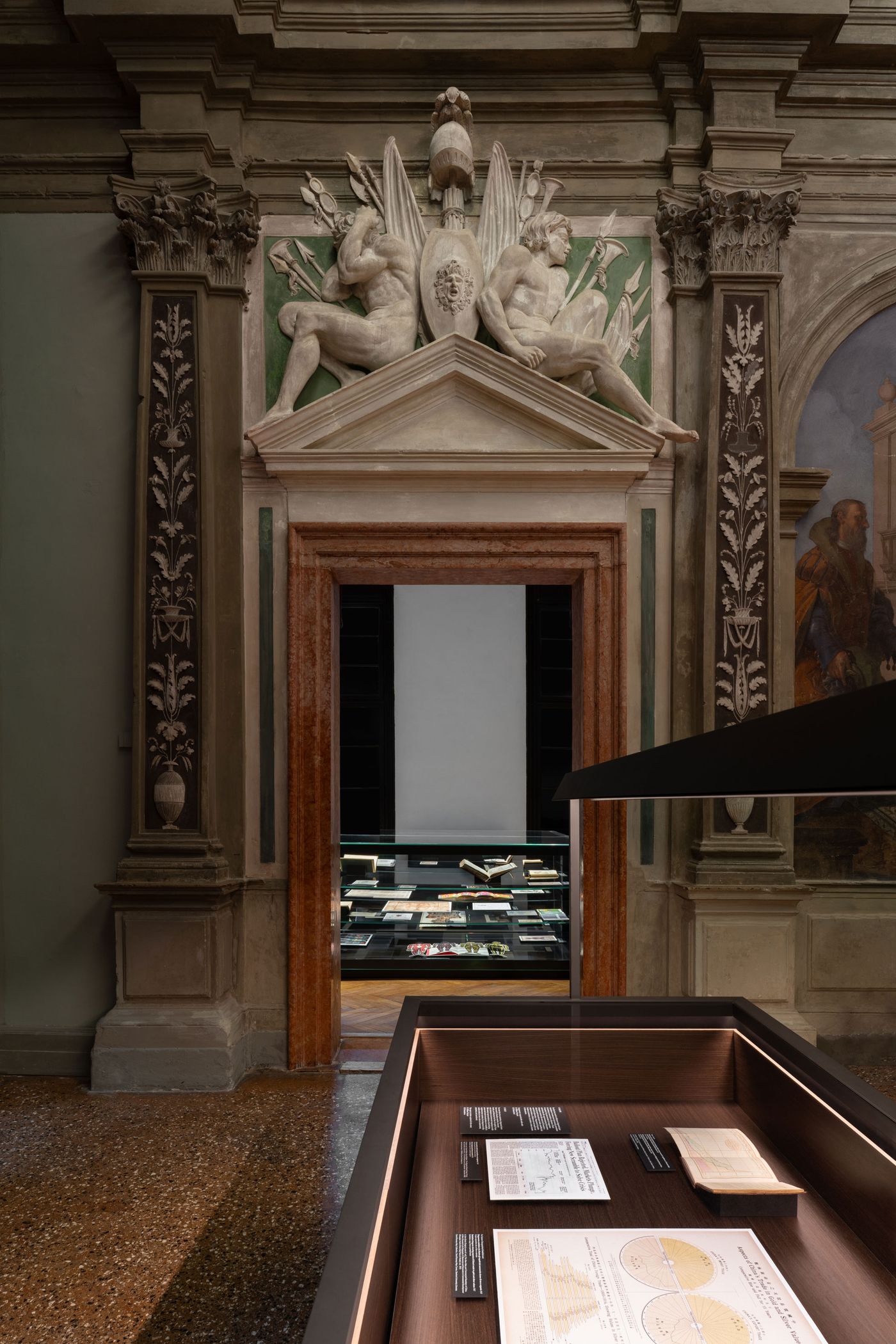 An ornate entrance leads to a dimly lit room filled with books, showcasing intricate architectural details and a display table.