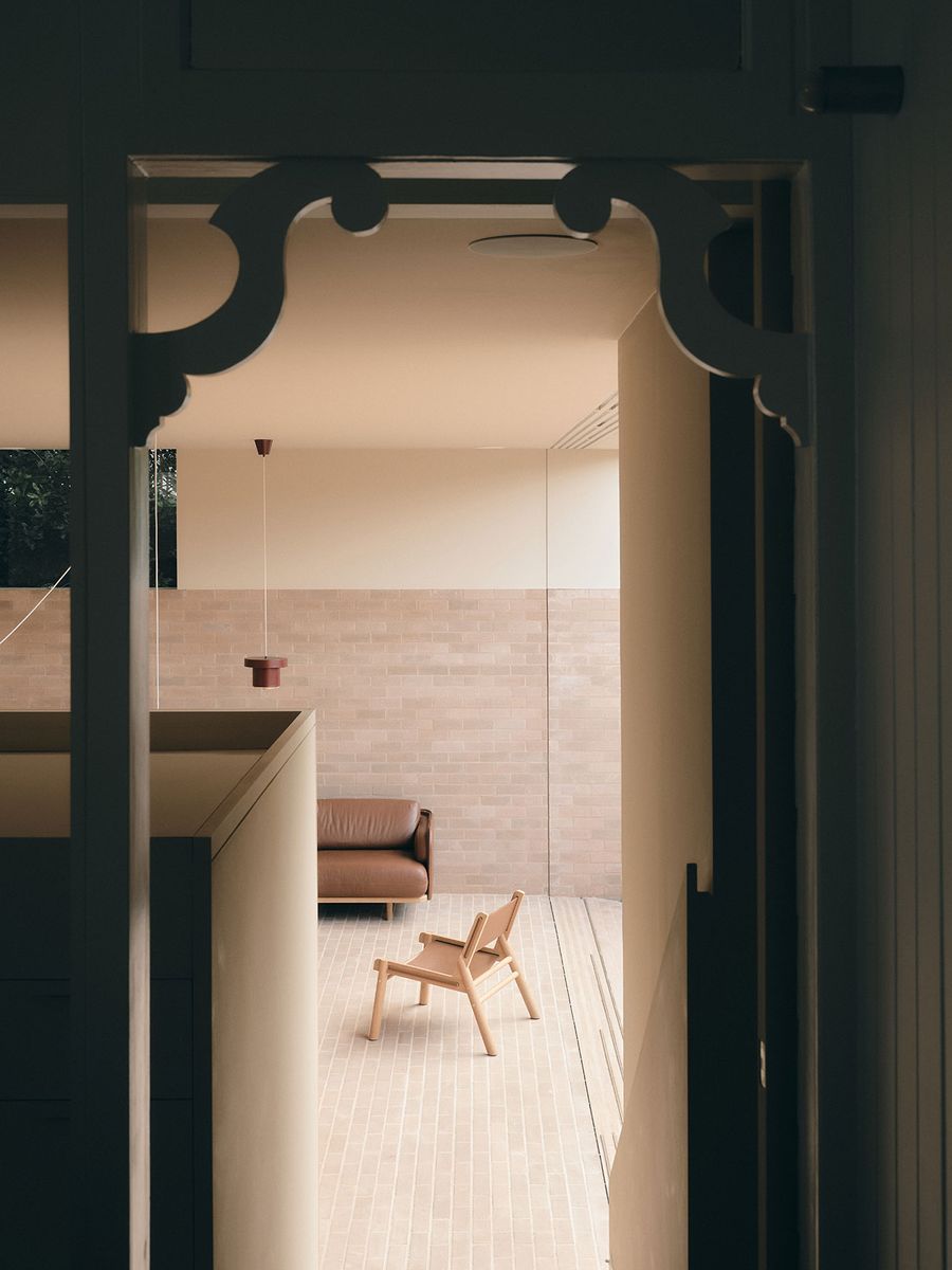 View through an ornate doorway into a minimalist, light-filled living space featuring a wooden chair and a brown leather sofa. View through an ornate doorway into a minimalist, light-filled living space featuring a wooden chair and a brown leather sofa.
