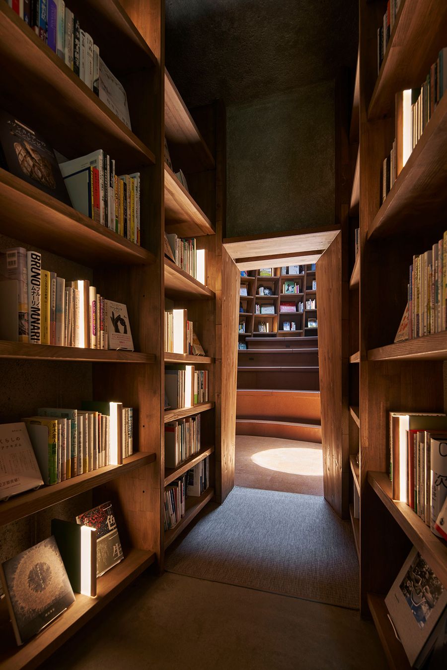 A cozy, illuminated passageway lined with wooden bookshelves leads to a circular reading area, inviting exploration and serenity. A cozy, illuminated passageway lined with wooden bookshelves leads to a circular reading area, inviting exploration and serenity.