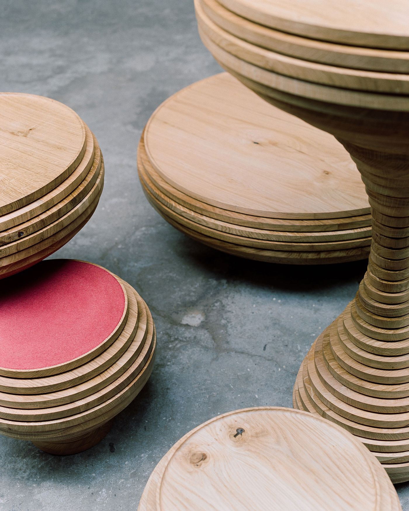 Laminated wood vessels reveal their construction through visible layers, creating sculptural seating or side tables with organic silhouettes. A pop of coral fabric adds warmth to the natural wood tones, demonstrating how traditional woodworking techniques can yield contemporary functional art pieces.