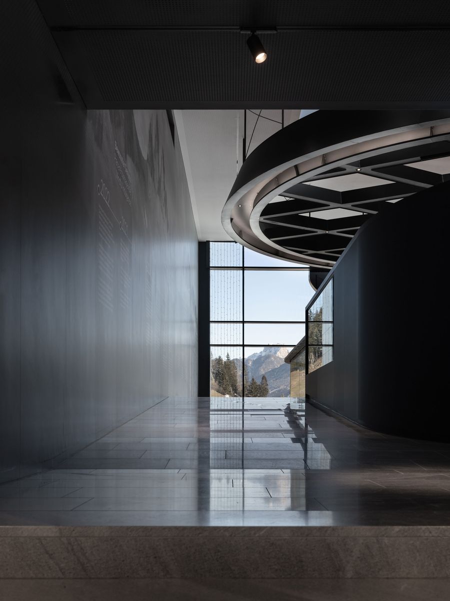 A dramatic curved staircase winds upward beneath a dark geometric ceiling structure, creating sculptural circulation through the space. The interplay between the organic stair form and rigid ceiling grid establishes dynamic tension, while polished surfaces reflect mountain views visible through expansive glazing. A dramatic curved staircase winds upward beneath a dark geometric ceiling structure, creating sculptural circulation through the space. The interplay between the organic stair form and rigid ceiling grid establishes dynamic tension, while polished surfaces reflect mountain views visible through expansive glazing.