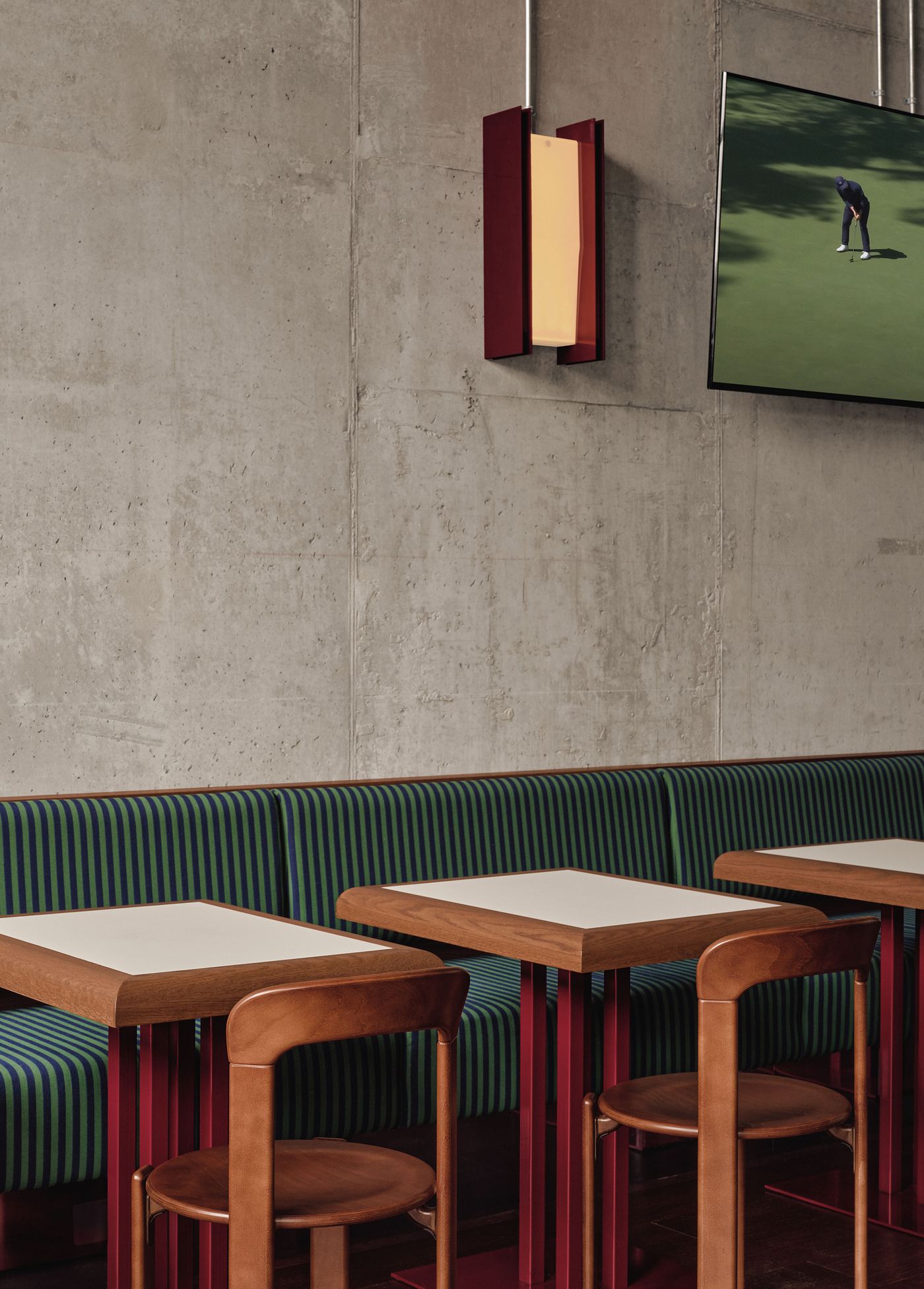 Cozy modern dining area featuring green-striped seating, wooden tables, and a stylish light fixture, with a TV displaying golf in the background.