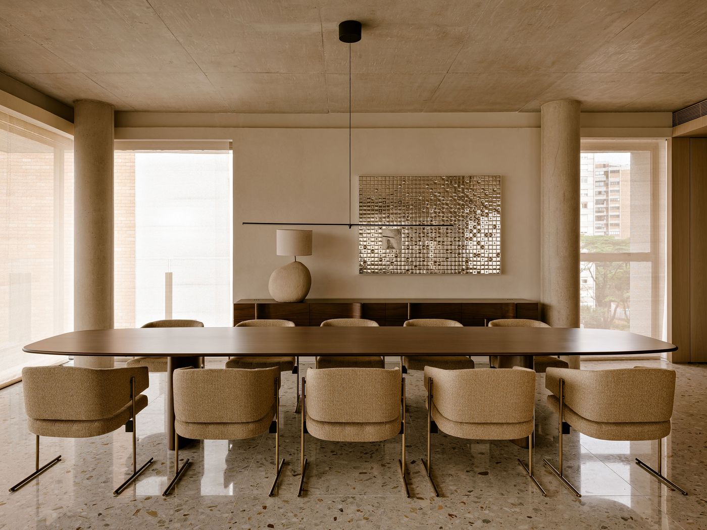 A modern dining area featuring a long wooden table, beige upholstered chairs, and a textured wall art, with natural light streaming through large windows. A modern dining area featuring a long wooden table, beige upholstered chairs, and a textured wall art, with natural light streaming through large windows.