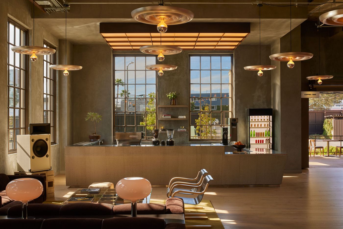 Bright, modern office lounge with large windows, stylish furniture, and greenery, featuring hanging lights and a sleek coffee bar. Bright, modern office lounge with large windows, stylish furniture, and greenery, featuring hanging lights and a sleek coffee bar.