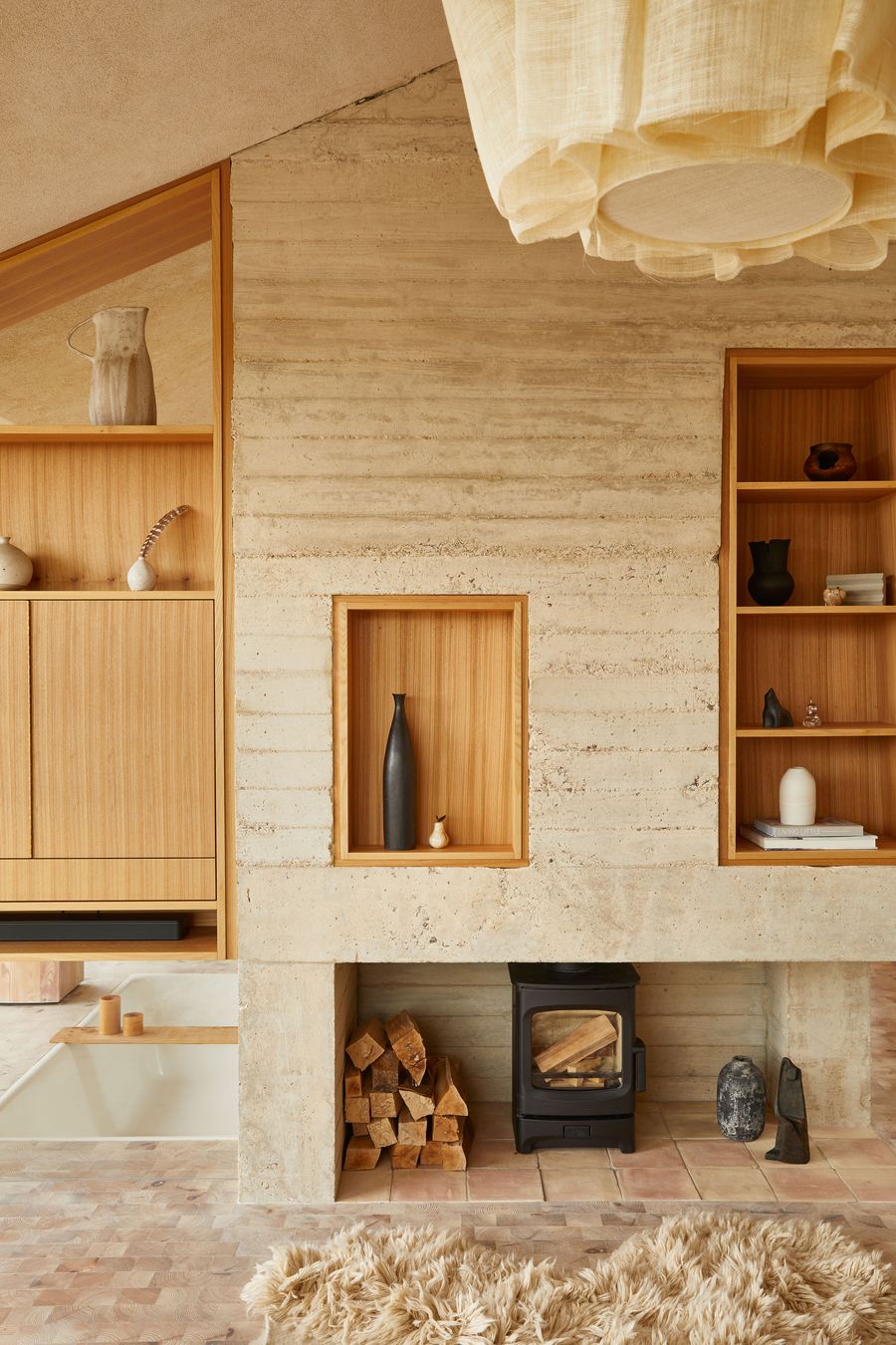 This close-up within The Maker's Barn highlights its material richness and craftsmanship. A prominent rammed earth wall serves as a central feature, integrating a modern wood-burning stove and bespoke timber shelving with artful displays. The contrasting textures of the wall, light wood cabinetry, and a plush, light-colored sheepskin rug create a warm, inviting, and highly tactile atmosphere. This close-up within The Maker's Barn highlights its material richness and craftsmanship. A prominent rammed earth wall serves as a central feature, integrating a modern wood-burning stove and bespoke timber shelving with artful displays. The contrasting textures of the wall, light wood cabinetry, and a plush, light-colored sheepskin rug create a warm, inviting, and highly tactile atmosphere.