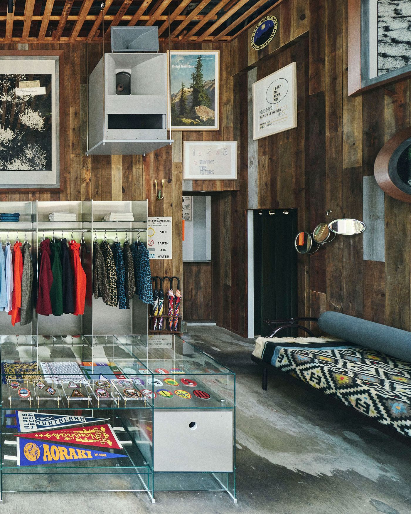 A stylish retail space with wooden walls, colorful clothing display, a clear showcase of stickers, and eclectic wall art and mirrors.