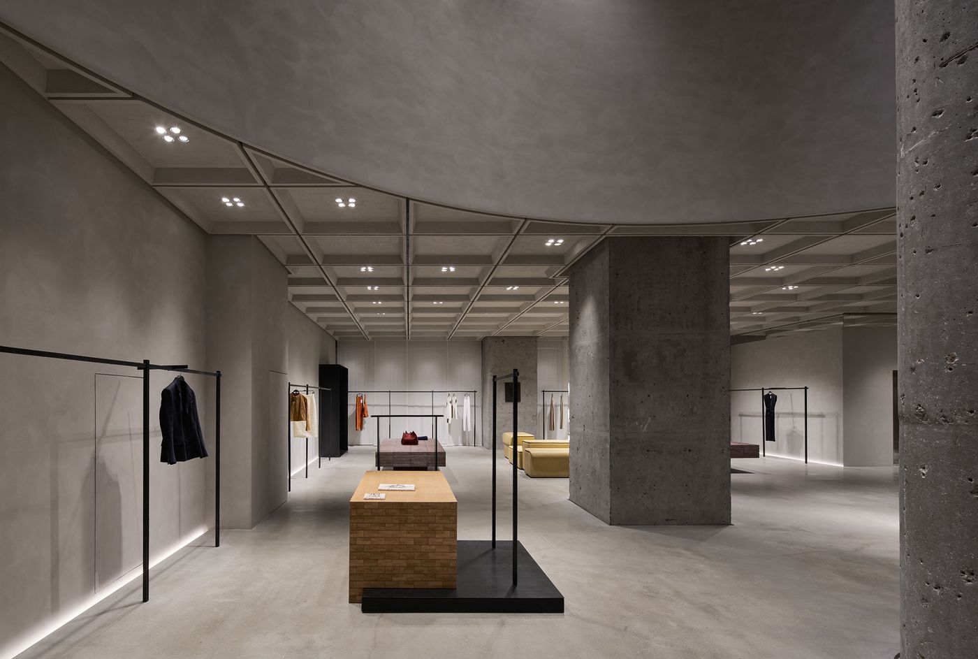 A modern clothing store interior featuring minimalist displays, concrete pillars, and soft lighting highlighting various garments. A modern clothing store interior featuring minimalist displays, concrete pillars, and soft lighting highlighting various garments.