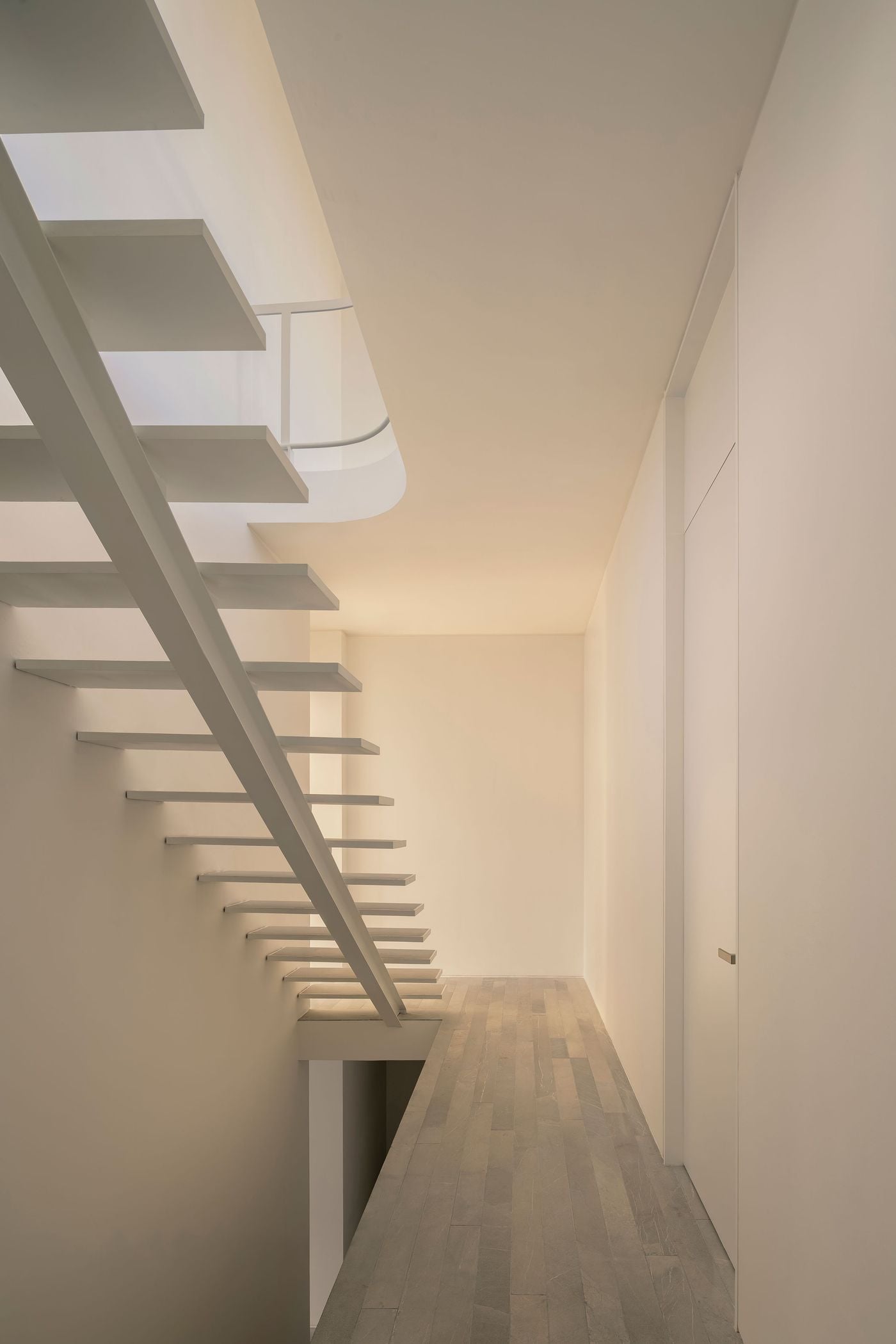 Casa Tlaloc’s open-riser staircase appears almost weightless from this side view, its slim treads projecting from a central spine beside the upper-floor corridor. White walls and concealed storage amplify the sense of restraint, while daylight filtering through the curved opening above gives the circulation space a soft, atmospheric glow. Casa Tlaloc’s open-riser staircase appears almost weightless from this side view, its slim treads projecting from a central spine beside the upper-floor corridor. White walls and concealed storage amplify the sense of restraint, while daylight filtering through the curved opening above gives the circulation space a soft, atmospheric glow.