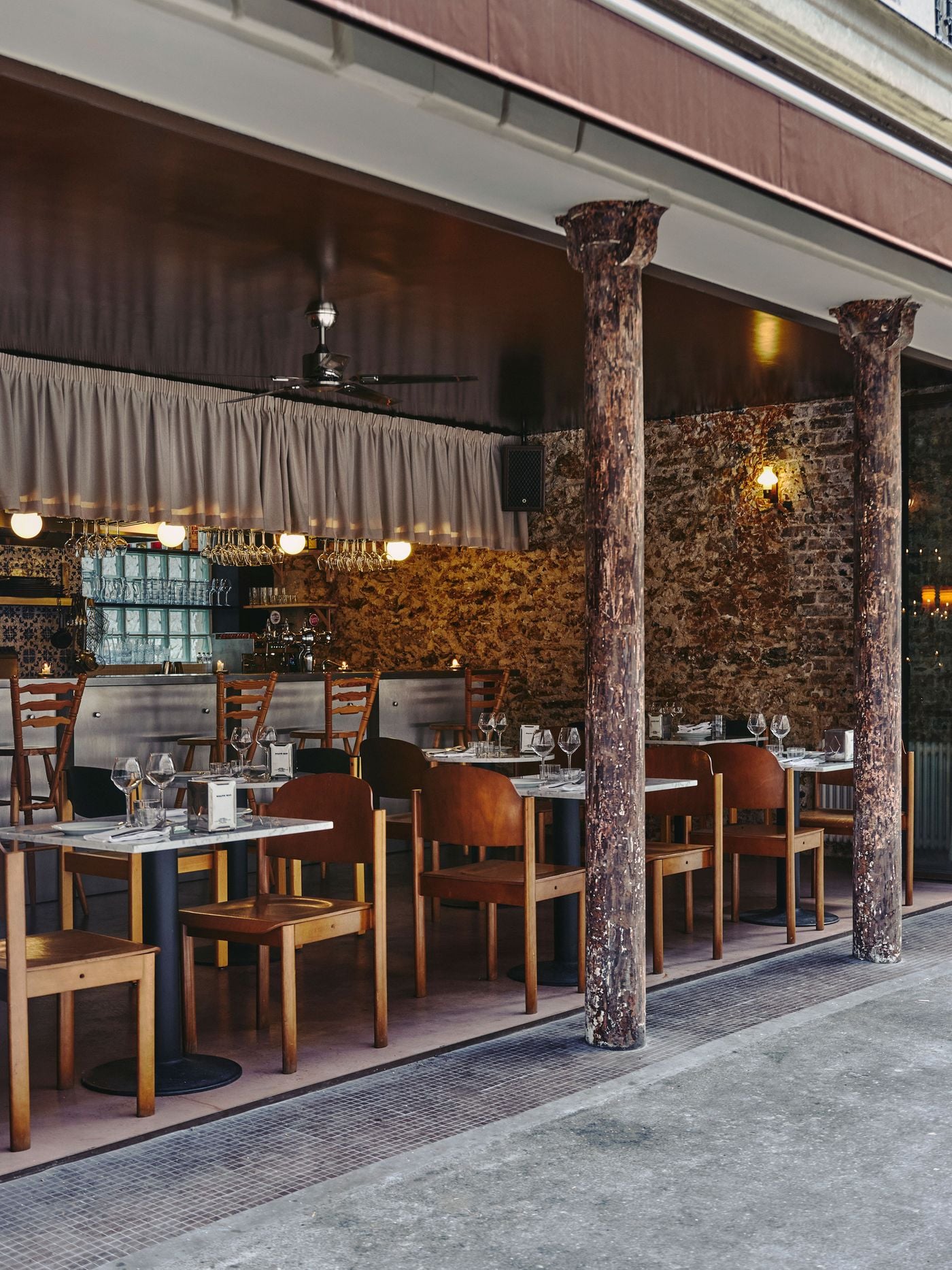 With its glazed frontage fully open, SaltoBar in Paris spills towards the pavement between two weathered cast-iron columns. Marble tables and warm wooden chairs sit on a mosaic-tiled threshold. Beyond them, the steel bar, pleated valance and glowing globe lights stand against a textured rubblestone wall. With its glazed frontage fully open, SaltoBar in Paris spills towards the pavement between two weathered cast-iron columns. Marble tables and warm wooden chairs sit on a mosaic-tiled threshold. Beyond them, the steel bar, pleated valance and glowing globe lights stand against a textured rubblestone wall.