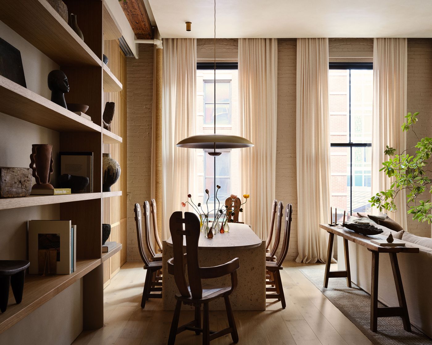A modern dining area featuring a wooden table, sculptural decor, and large windows with sheer curtains, creating a warm, inviting atmosphere. A modern dining area featuring a wooden table, sculptural decor, and large windows with sheer curtains, creating a warm, inviting atmosphere.