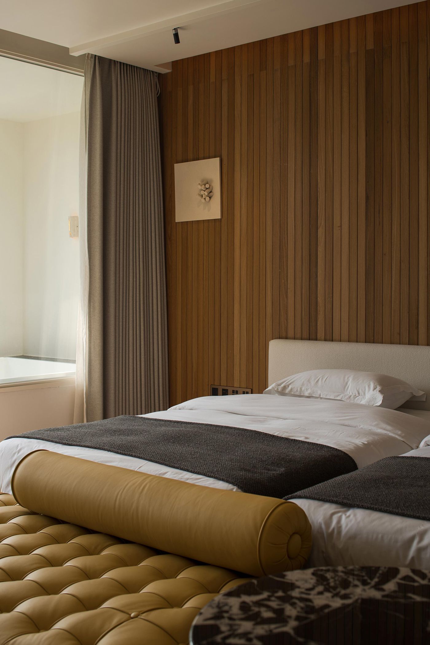 Cozy bedroom featuring a wooden accent wall, a plush yellow bolster, and soft gray bedding, illuminated by natural light from the window.