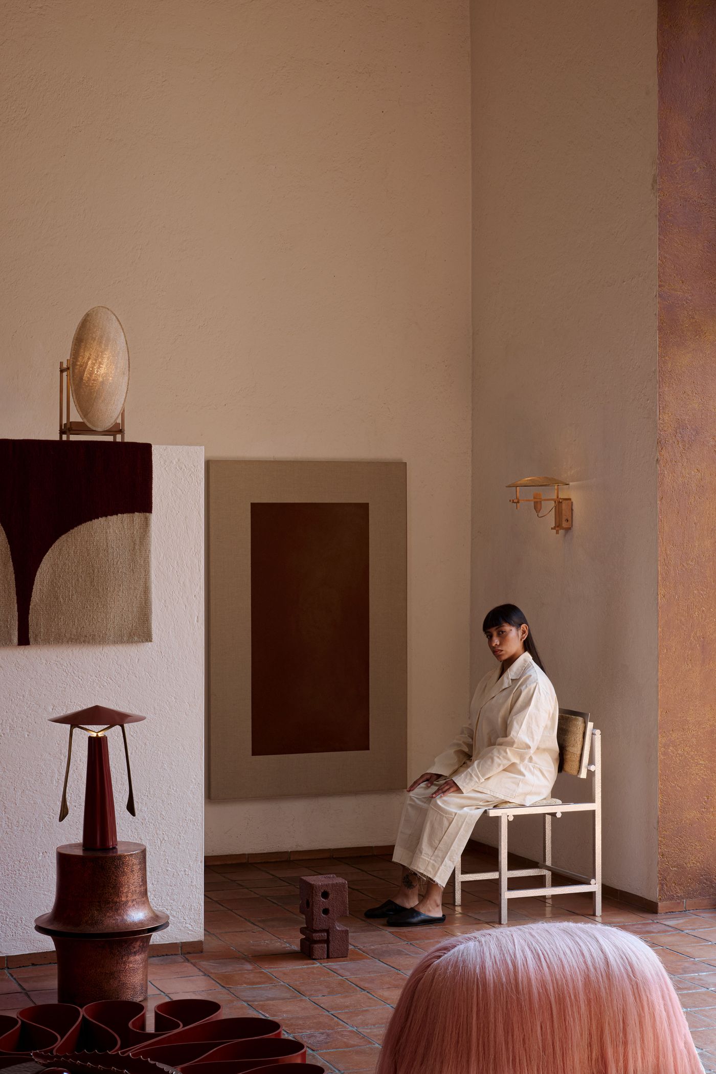 A serene interior setting featuring a woman in an elegant garment, surrounded by minimalist art and unique decor on textured walls.