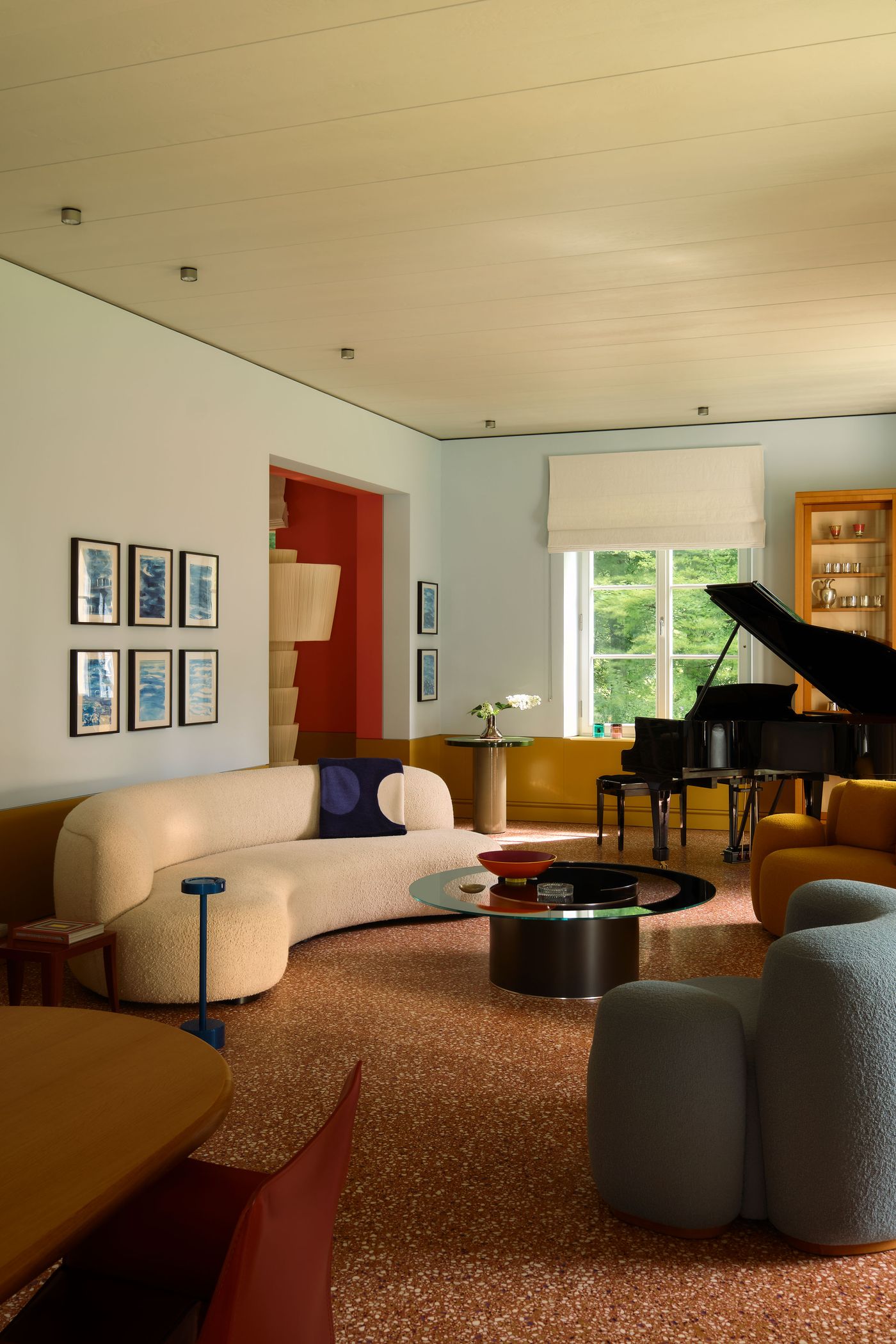 A stylish living room featuring a rounded beige sofa, colorful chairs, a grand piano, and vibrant wall art, well-lit by natural light. A stylish living room featuring a rounded beige sofa, colorful chairs, a grand piano, and vibrant wall art, well-lit by natural light.