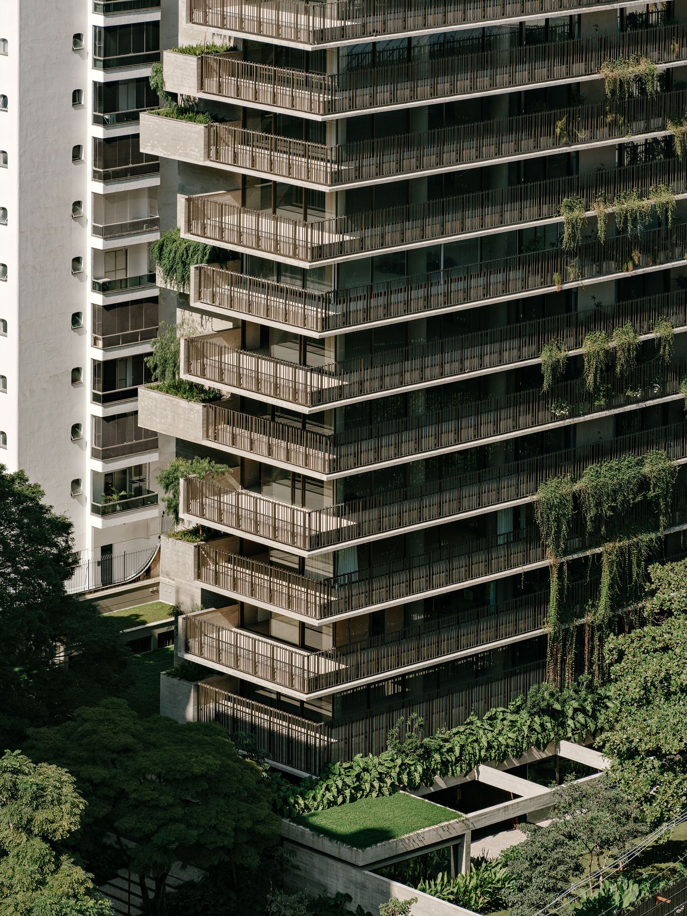 An aerial perspective captures the dynamic facade, where concrete balconies with vertical screens are lush with trailing green plants. The building's layered form integrates seamlessly with the surrounding mature trees and green rooftops, showcasing a biophilic approach to high-rise living in São Paulo. An aerial perspective captures the dynamic facade, where concrete balconies with vertical screens are lush with trailing green plants. The building's layered form integrates seamlessly with the surrounding mature trees and green rooftops, showcasing a biophilic approach to high-rise living in São Paulo.