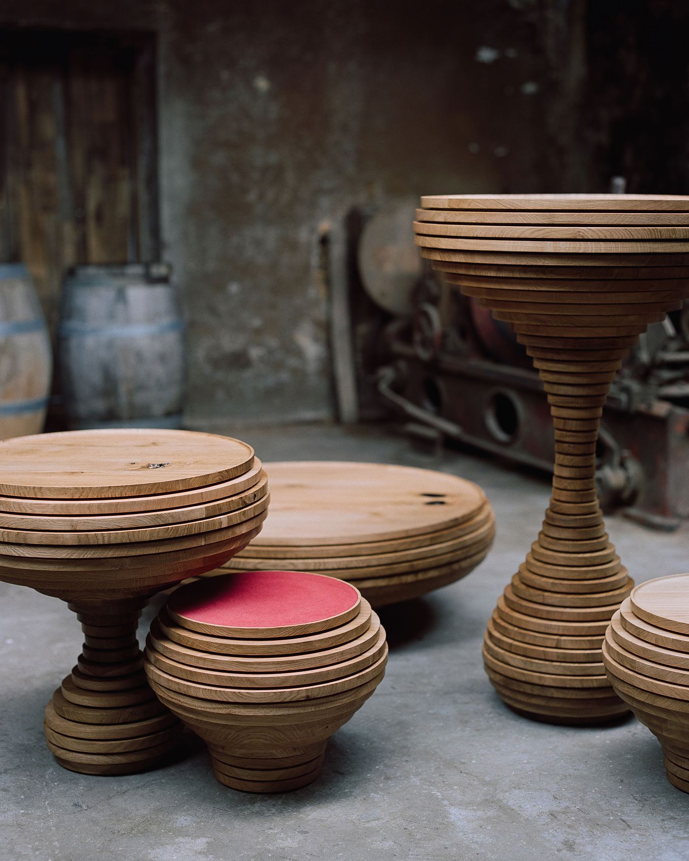 The workshop environment frames these sculptural wooden pieces as works in progress, their turned profiles creating dynamic shadows on polished concrete. The industrial backdrop emphasizes the transformation from raw material to refined object, celebrating the alchemy of traditional craftsmanship in modern making.