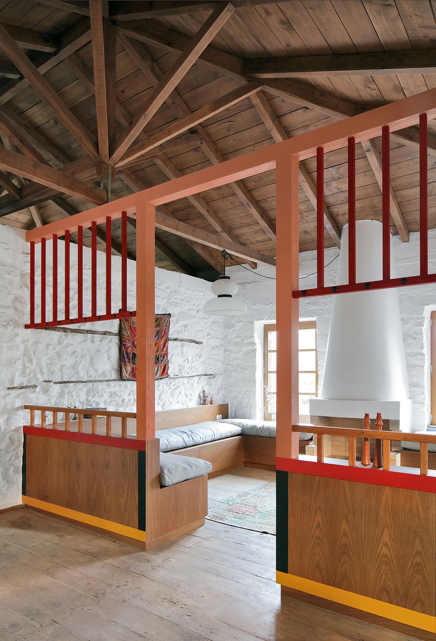 Geometric coral-red steel frameworks create spatial hierarchy within the restored stone shell, where traditional timber roof construction meets contemporary mezzanine insertions. The modular sleeping arrangement transforms the historic interior into a flexible communal space emphasizing both privacy and connection.