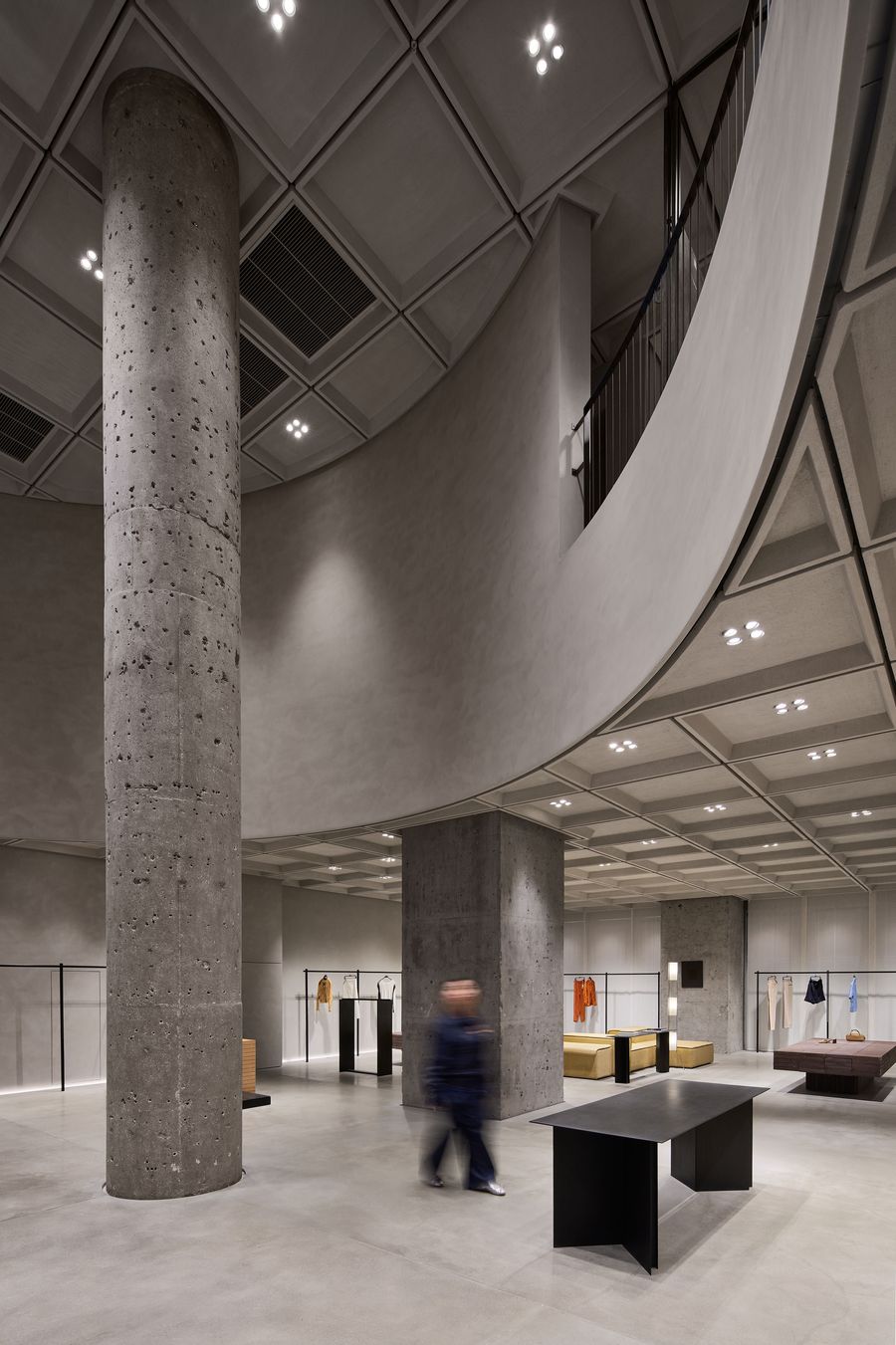 Minimalist clothing store interior with large concrete pillars, sleek furniture, and hanging garments, featuring modern lighting. Minimalist clothing store interior with large concrete pillars, sleek furniture, and hanging garments, featuring modern lighting.