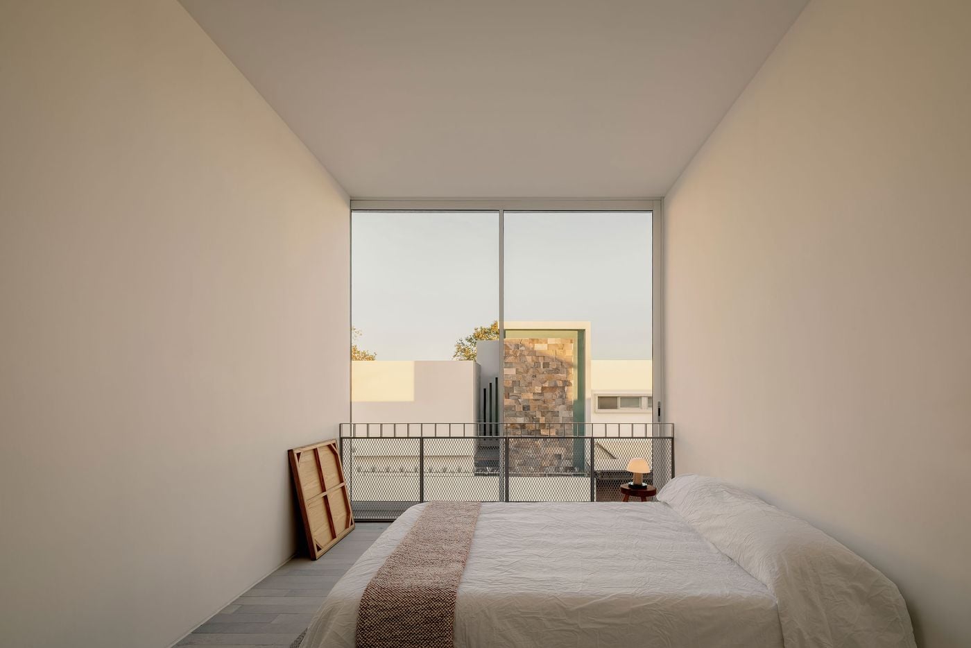 A bedroom at Casa Tlaloc is reduced to essential elements: white walls, pale grey flooring and an unadorned bed facing a wall of floor-to-ceiling glass. Beyond, a metal-mesh balustrade and neighbouring architecture become part of the composition, allowing the exterior view to provide much of the room’s visual character. A bedroom at Casa Tlaloc is reduced to essential elements: white walls, pale grey flooring and an unadorned bed facing a wall of floor-to-ceiling glass. Beyond, a metal-mesh balustrade and neighbouring architecture become part of the composition, allowing the exterior view to provide much of the room’s visual character.