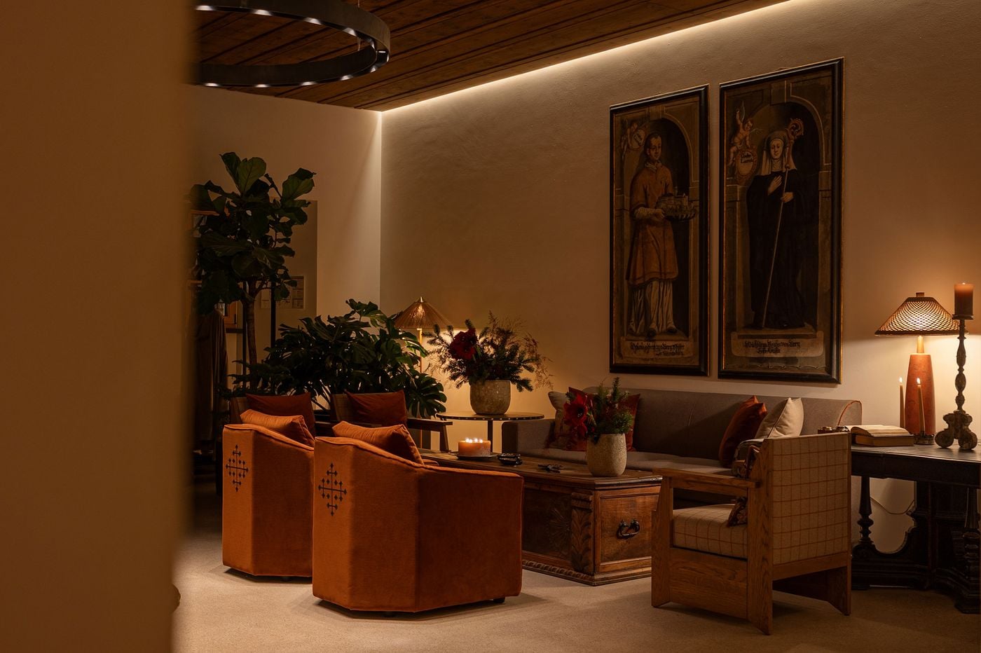 Two tall historic portraits preside over a lounge at Castel Badia: a man holding a model of the castle and an abbess with a crozier. Below, rust velvet armchairs embroidered with cross motifs and a plaid-upholstered timber armchair surround a carved antique chest, softened by amaryllis, foliage and woven lampshades. Two tall historic portraits preside over a lounge at Castel Badia: a man holding a model of the castle and an abbess with a crozier. Below, rust velvet armchairs embroidered with cross motifs and a plaid-upholstered timber armchair surround a carved antique chest, softened by amaryllis, foliage and woven lampshades.