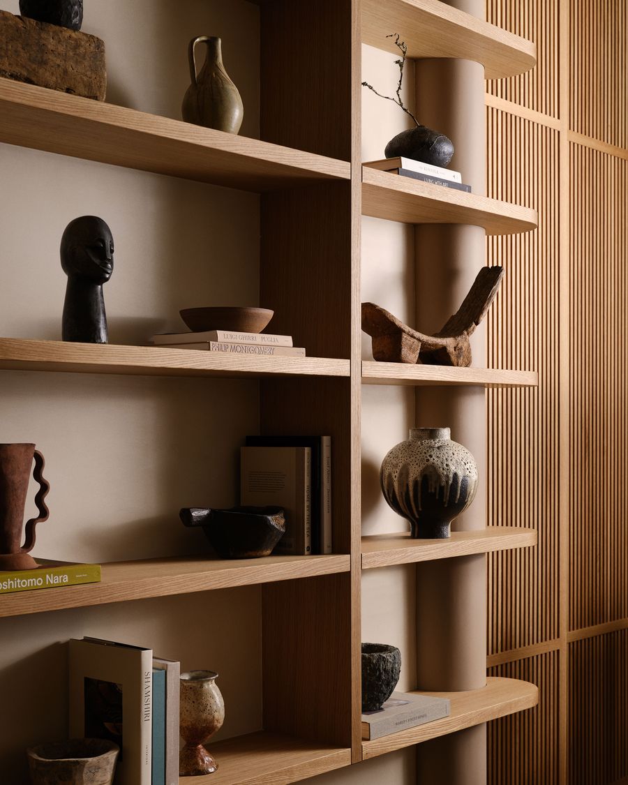 A stylish shelf filled with various ceramic pots, a wooden sculpture, and stacked books against a warm, neutral background. A stylish shelf filled with various ceramic pots, a wooden sculpture, and stacked books against a warm, neutral background.