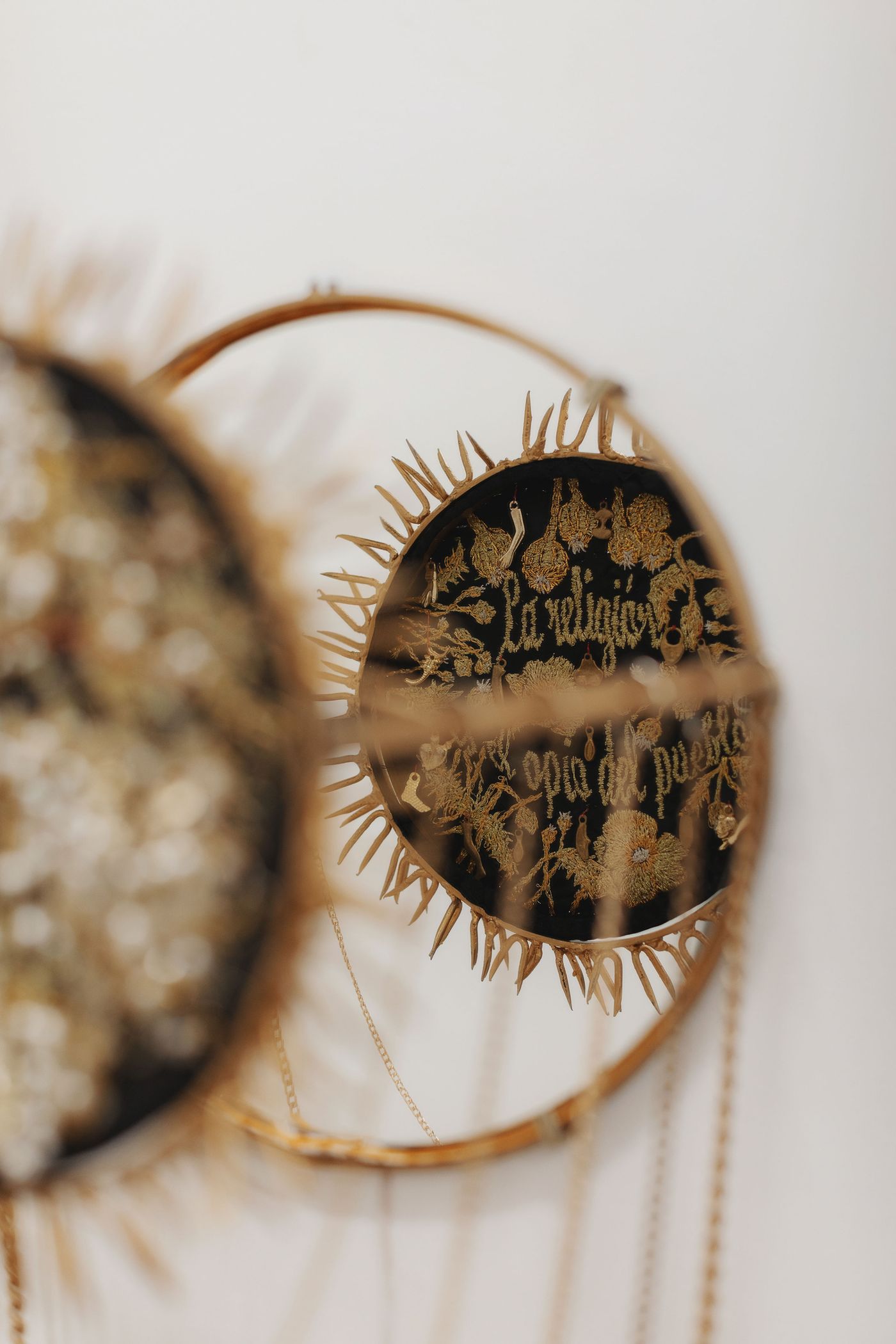 Close-up of a decorative wall hanging featuring intricate golden flora and fauna designs on a dark background, with a sun-like border.
