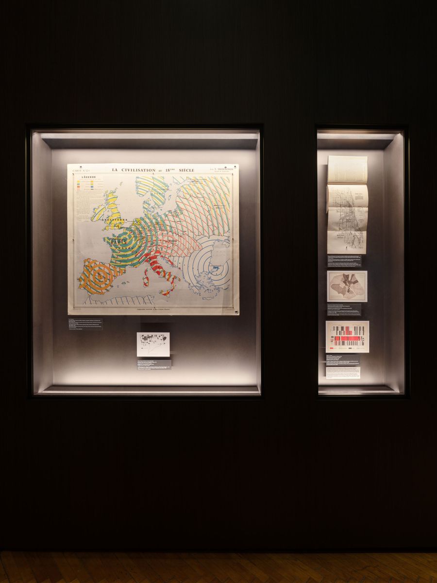 A historic map of Europe labeled "La Civilisation au 18ème Siècle," displayed in a dark exhibit case with additional documents. A historic map of Europe labeled "La Civilisation au 18ème Siècle," displayed in a dark exhibit case with additional documents.