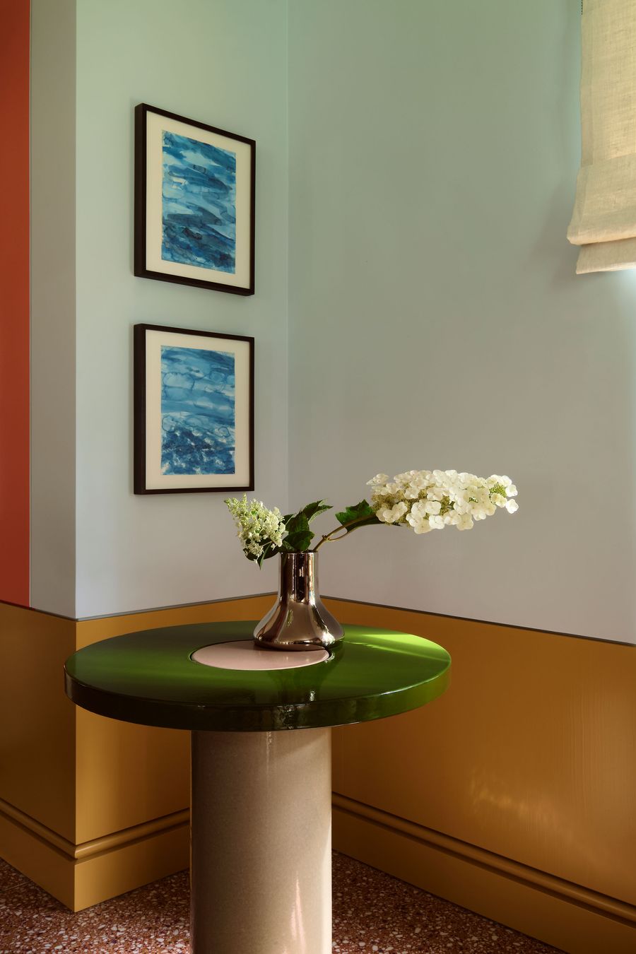 A stylish interior featuring a green table, metallic vase with white flowers, and blue abstract artwork on the walls. Soft, colorful palette. A stylish interior featuring a green table, metallic vase with white flowers, and blue abstract artwork on the walls. Soft, colorful palette.
