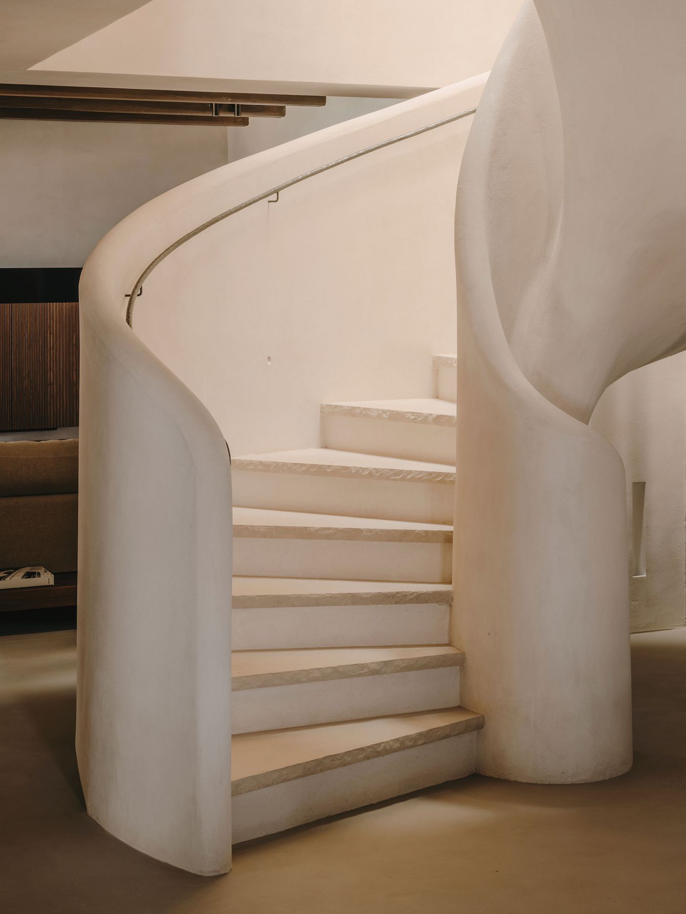 A beautifully designed spiral staircase with smooth, light-colored steps and curved walls, leading to an upper level in a modern setting.