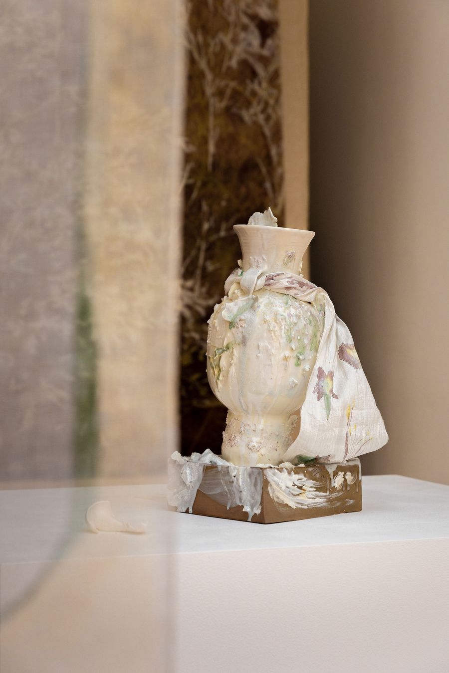 A distinctive sculptural piece by Bryon Studios, showcased during Lisbon Design Week, combines ceramic and textile elements. An organic, textured white vase appears to melt onto a brown base, adorned with a draped fabric featuring subtle floral motifs. The raw, almost deconstructed aesthetic offers a unique blend of fragility and artistic expression. A distinctive sculptural piece by Bryon Studios, showcased during Lisbon Design Week, combines ceramic and textile elements. An organic, textured white vase appears to melt onto a brown base, adorned with a draped fabric featuring subtle floral motifs. The raw, almost deconstructed aesthetic offers a unique blend of fragility and artistic expression.