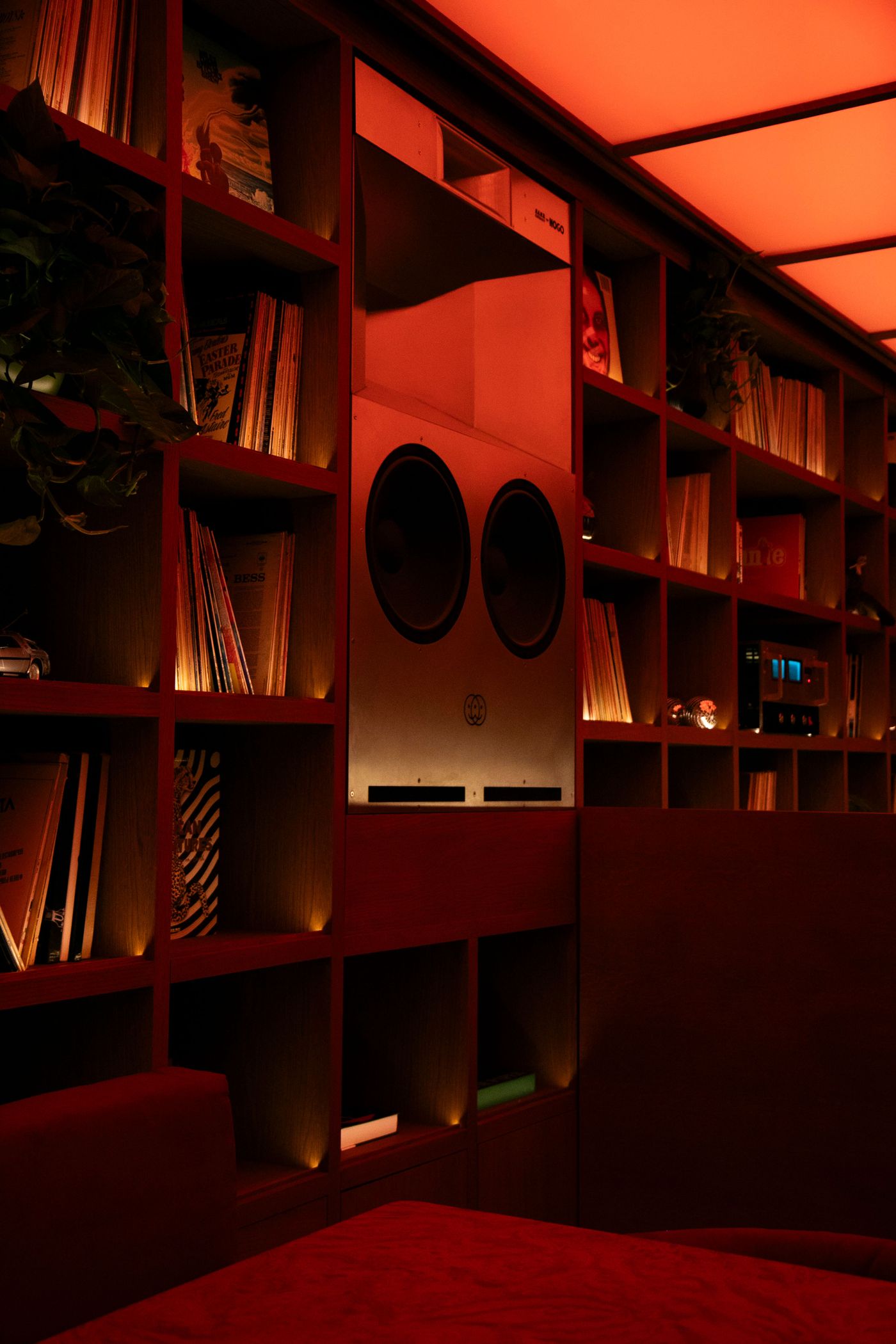 A cozy interior with red lighting, featuring a vintage sound system, vinyl records, and a plush red couch in a stylish bookshelf setting.