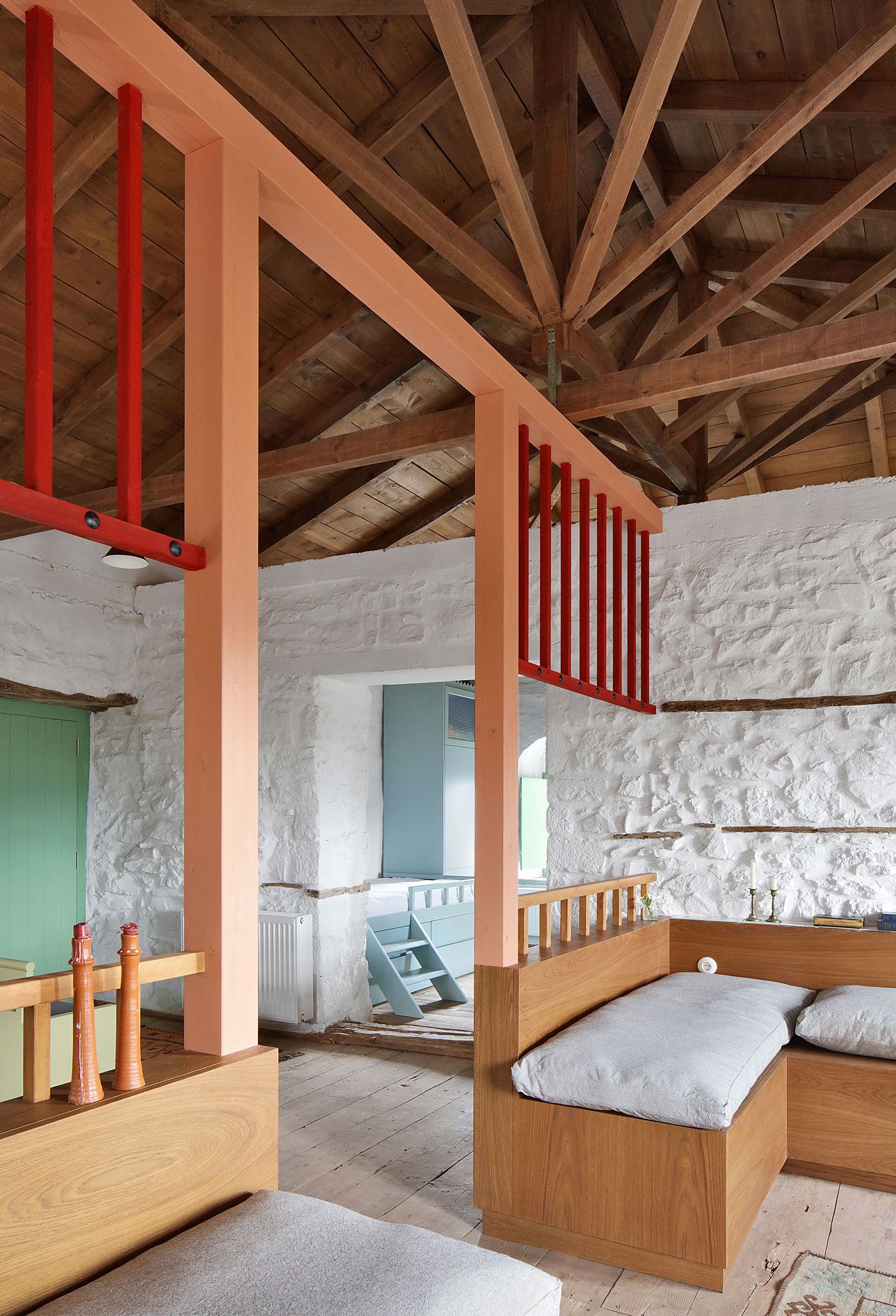 Contemporary coral and salmon-toned steel interventions create bold contrast against the ancient whitewashed stone interior. The multi-level sleeping arrangement demonstrates how modern elements can enhance rather than compete with historical architecture, establishing new spatial relationships within the preserved shell.