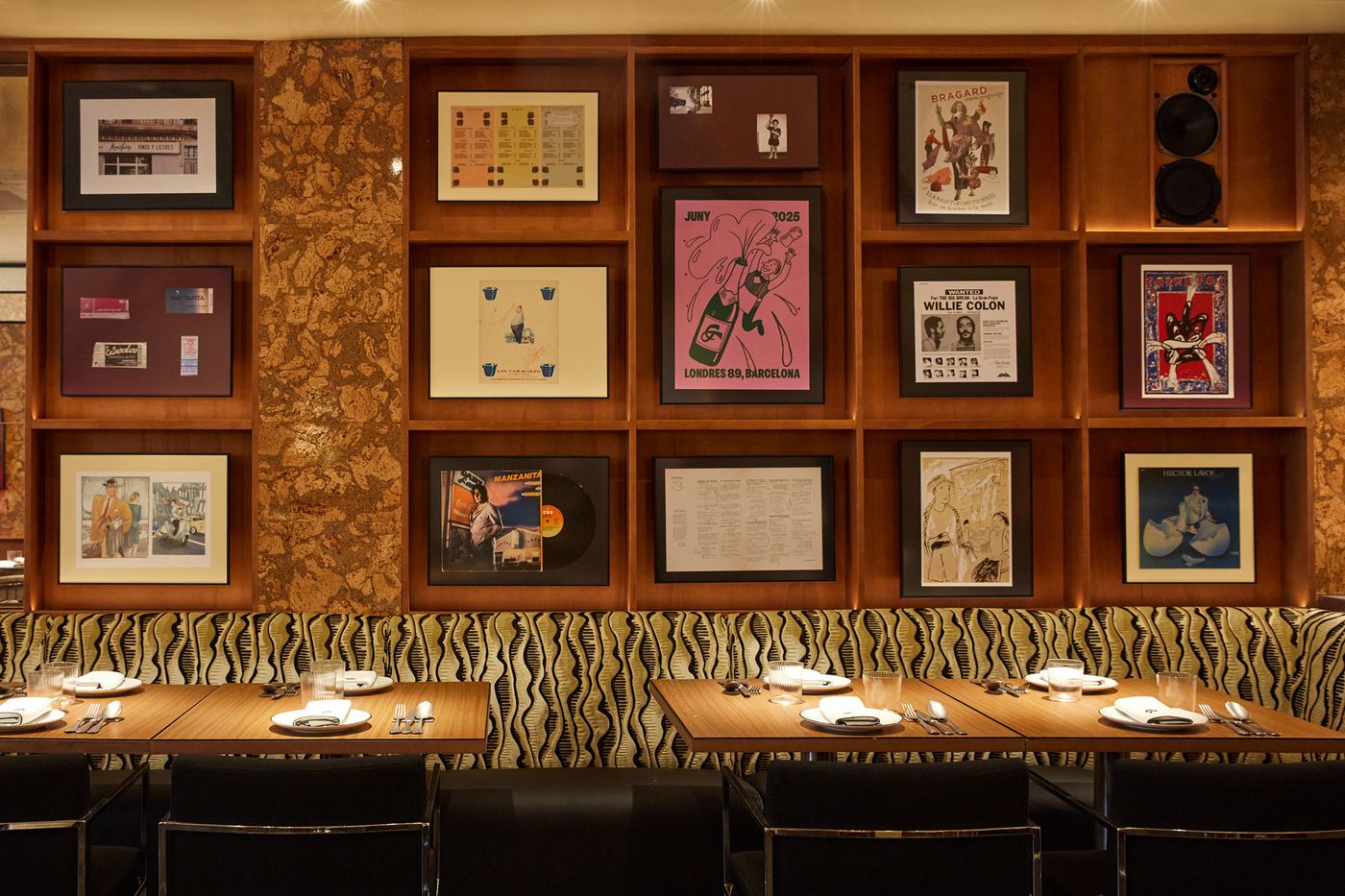 A well-composed wide shot of a dining space showcasing a striking gallery wall. The dark wooden shelving unit contains an assortment of framed posters, records, and photographs. The lively patterned seating below and simple wooden tables with black chairs complete the cohesive and visually rich aesthetic. A well-composed wide shot of a dining space showcasing a striking gallery wall. The dark wooden shelving unit contains an assortment of framed posters, records, and photographs. The lively patterned seating below and simple wooden tables with black chairs complete the cohesive and visually rich aesthetic.