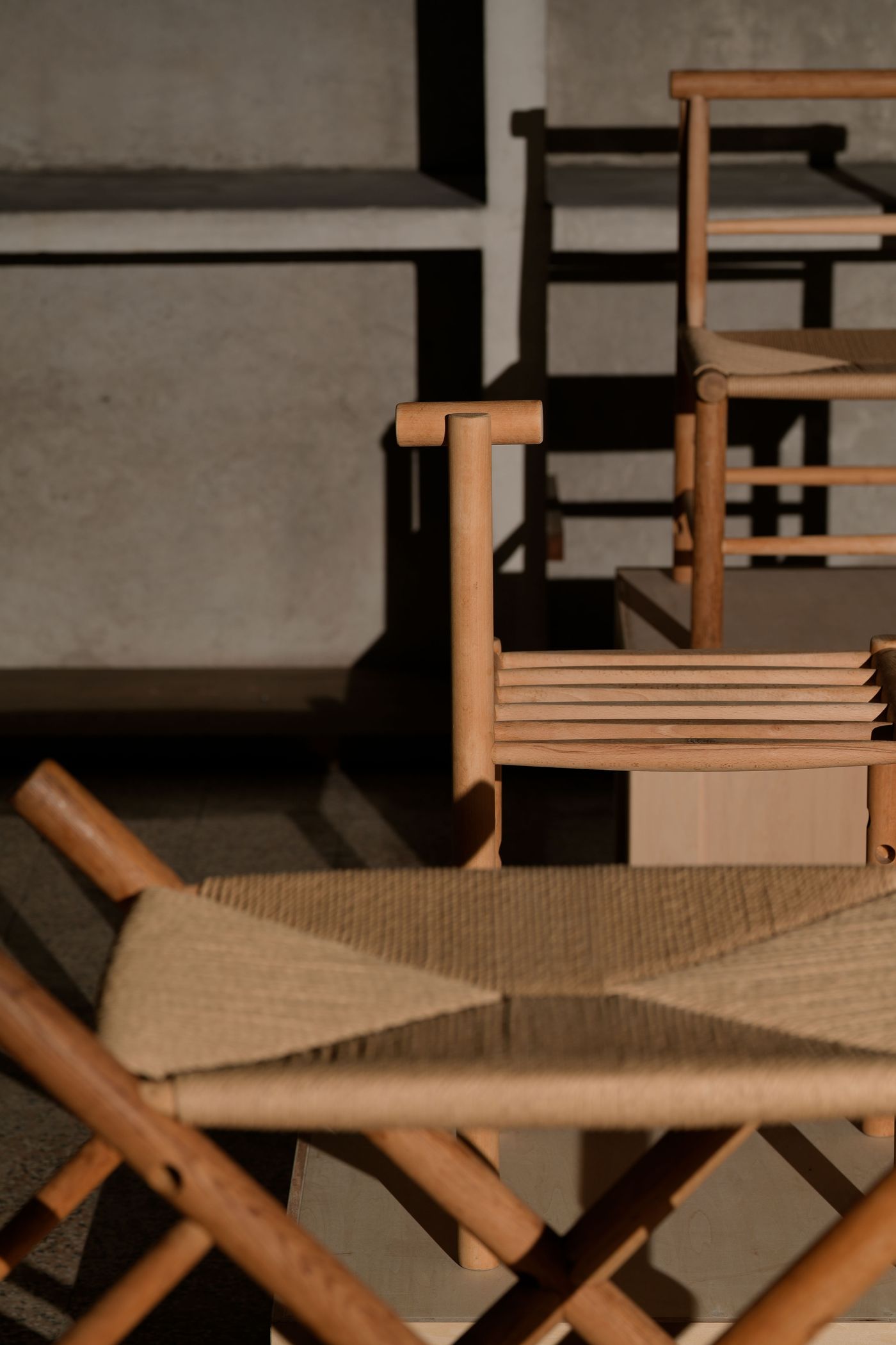 A collection of wooden chairs with natural textures, showcasing minimalistic design against a textured wall and soft shadows.