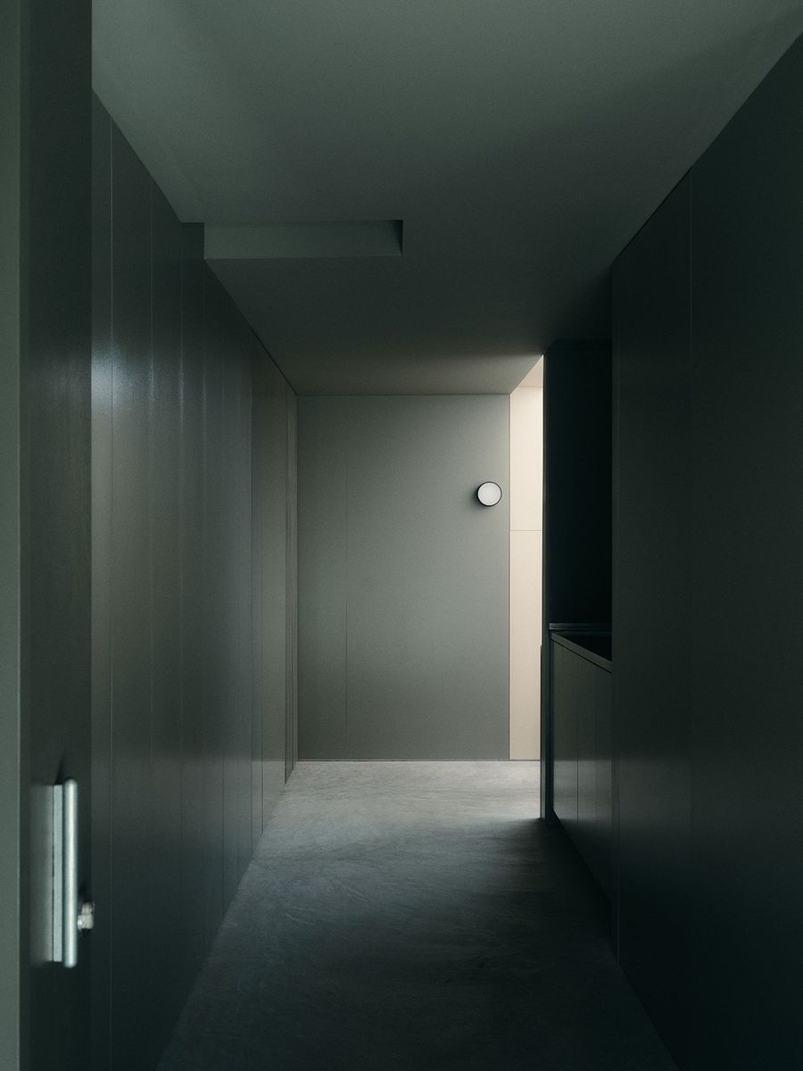 A minimalist hallway features dark gray walls, a round light fixture, and a faintly illuminated section at the end. A minimalist hallway features dark gray walls, a round light fixture, and a faintly illuminated section at the end.