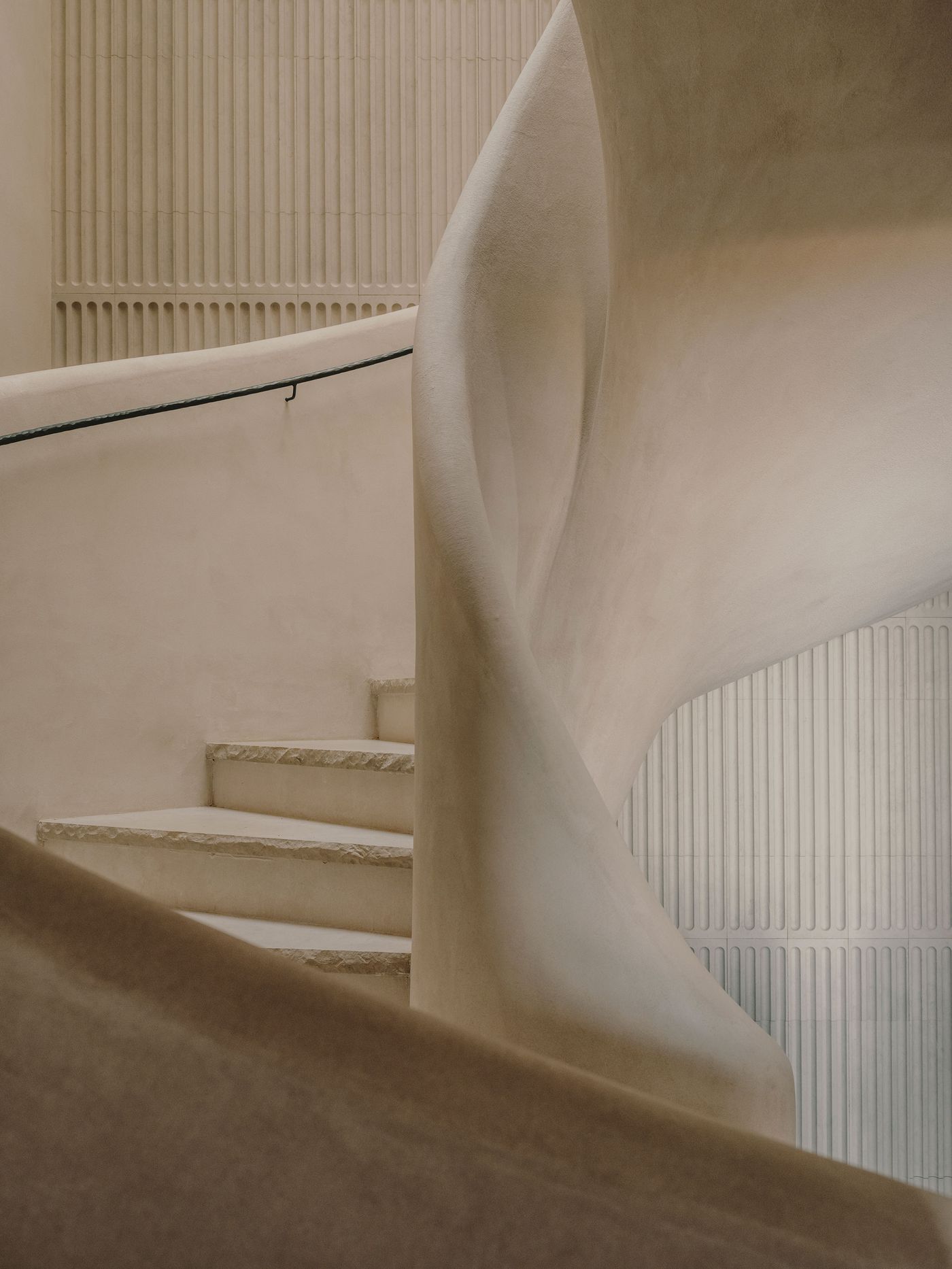 Curved, textured staircase with smooth walls and a ridged vertical panel, creating a modern, serene ambiance.