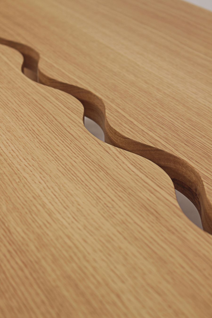 A close-up detail of a wooden table by Gonçalo Campos highlights a distinctive, undulating carved channel running across its light-toned surface. The fluid, organic groove contrasts with the straight grain of the wood, showcasing precise craftsmanship and a focus on subtle, sculptural details within a minimalist aesthetic. A close-up detail of a wooden table by Gonçalo Campos highlights a distinctive, undulating carved channel running across its light-toned surface. The fluid, organic groove contrasts with the straight grain of the wood, showcasing precise craftsmanship and a focus on subtle, sculptural details within a minimalist aesthetic.