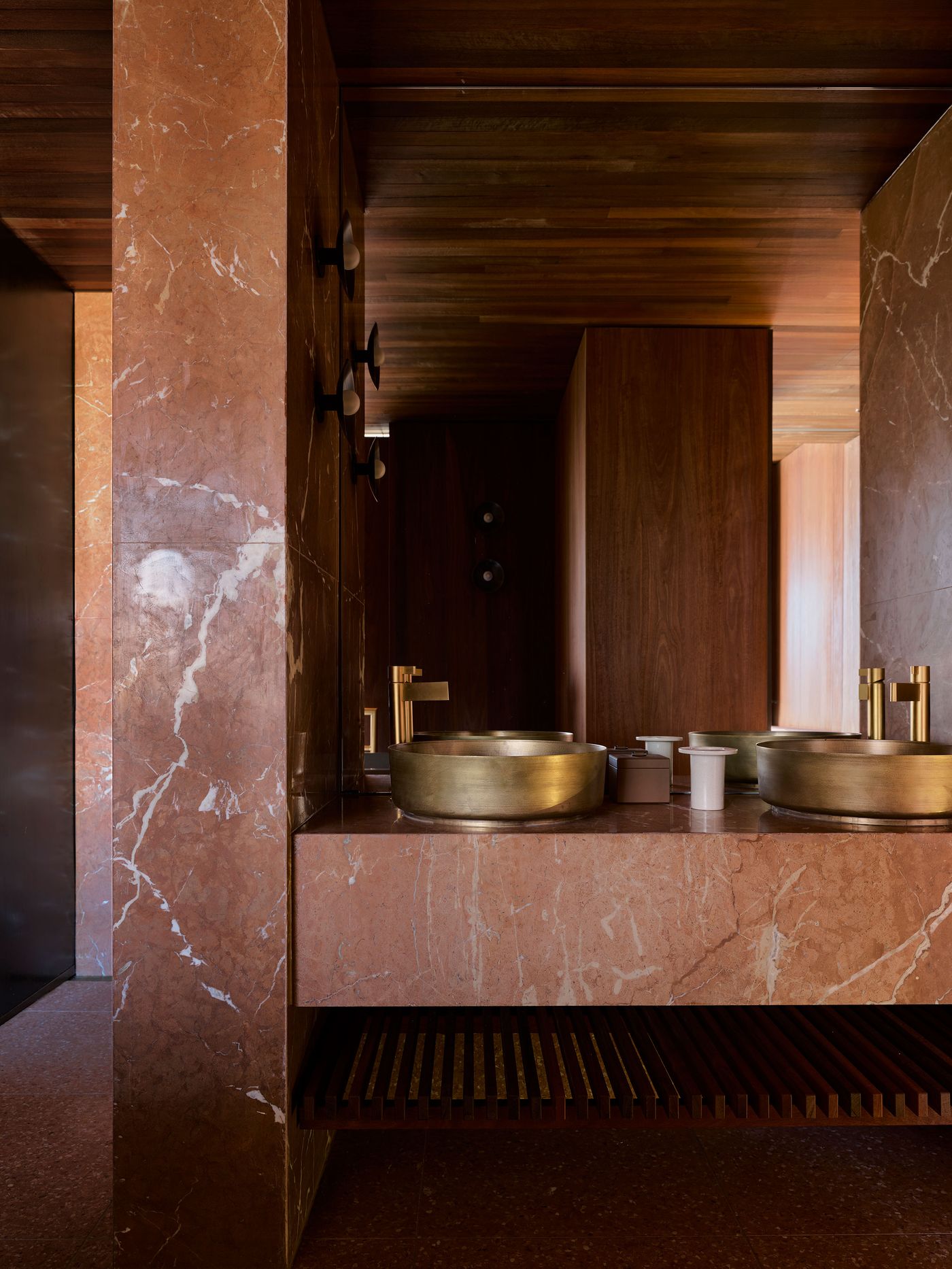 Luxurious bathroom with a pink marble vanity, brass sinks, and wooden accents, creating a warm modern aesthetic. Luxurious bathroom with a pink marble vanity, brass sinks, and wooden accents, creating a warm modern aesthetic.