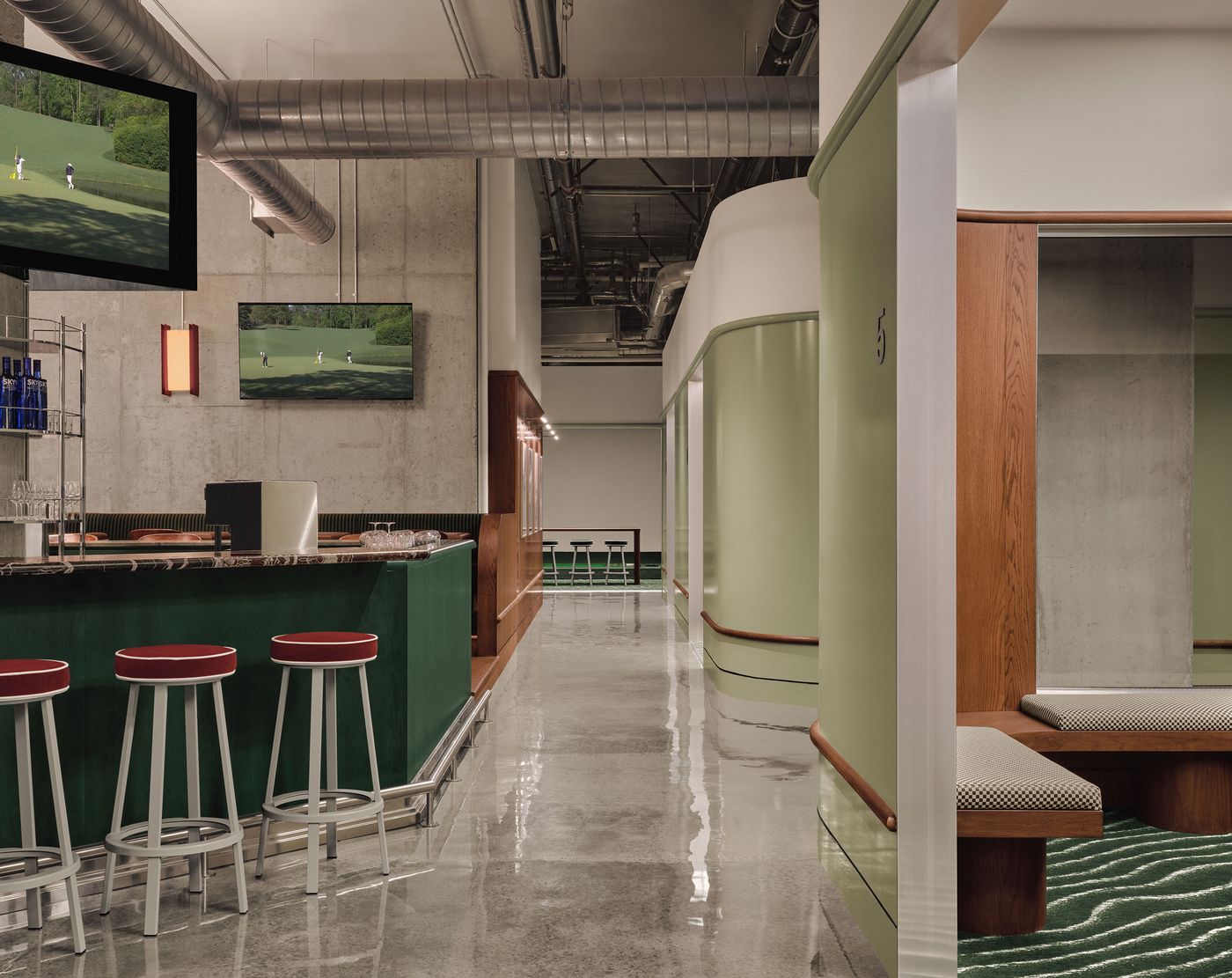 Modern indoor golf facility featuring a sleek bar, green walls, and a cozy seating area, accented by sports screens displaying golf. Modern indoor golf facility featuring a sleek bar, green walls, and a cozy seating area, accented by sports screens displaying golf.