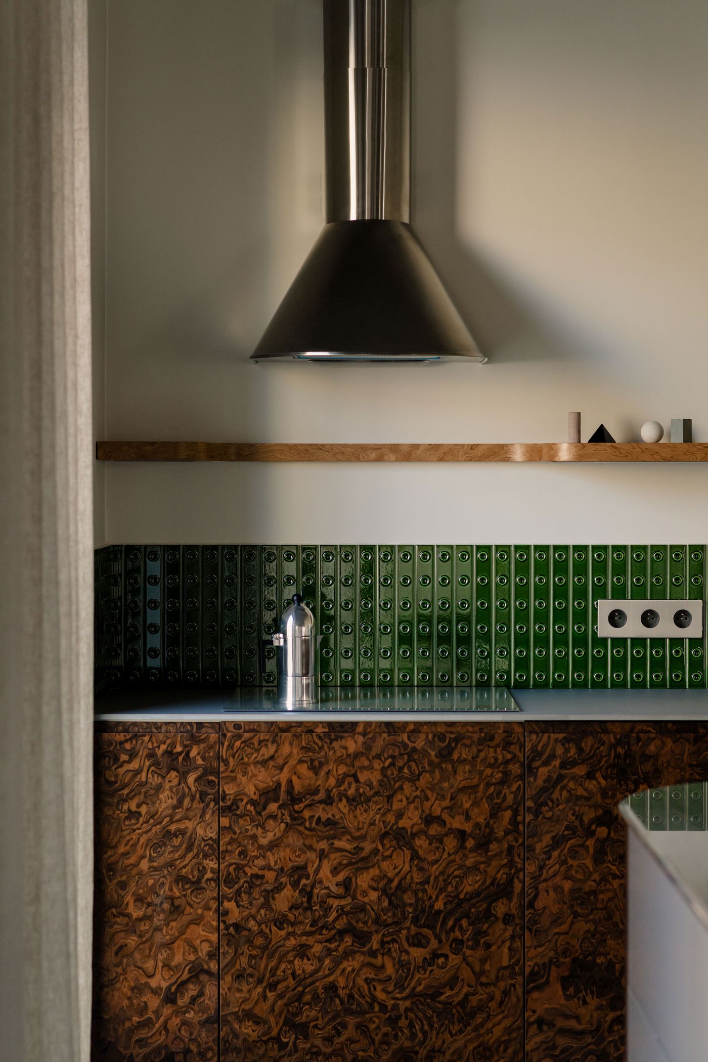 This cropped composition focuses on the dramatic conical range hood and horizontal shelf above the tactile green tile. Each element, from tile to vent, reinforces the kitchen’s industrial-poetic aesthetic. This cropped composition focuses on the dramatic conical range hood and horizontal shelf above the tactile green tile. Each element, from tile to vent, reinforces the kitchen’s industrial-poetic aesthetic.