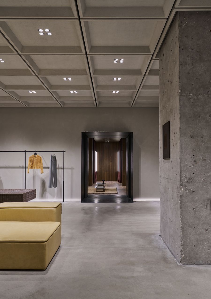 A minimalist retail space featuring concrete walls, stylish clothing displays, and a wooden-paneled entrance at the rear. A minimalist retail space featuring concrete walls, stylish clothing displays, and a wooden-paneled entrance at the rear.