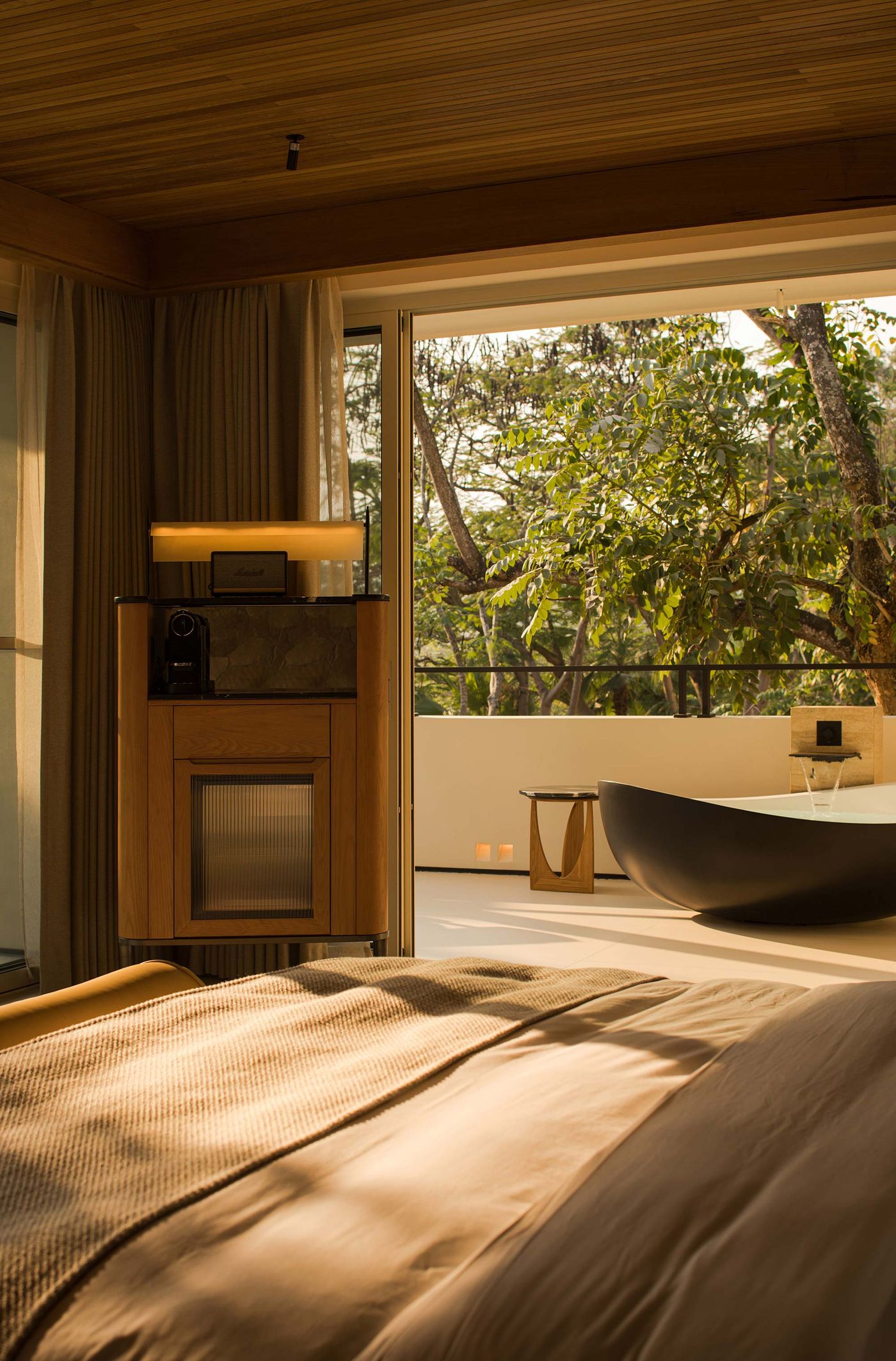 A modern bedroom with warm lighting, featuring a cozy bed, stylish cabinet, and a serene outdoor view with a black bathtub and greenery. A modern bedroom with warm lighting, featuring a cozy bed, stylish cabinet, and a serene outdoor view with a black bathtub and greenery.