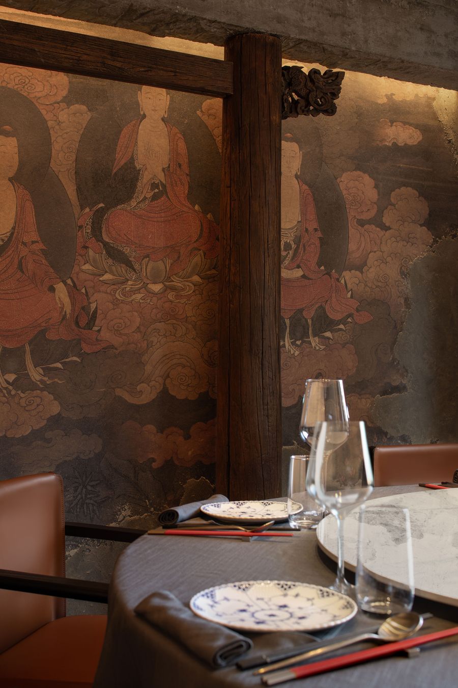 A restaurant setting featuring a beautifully decorated wall with traditional artwork, a round table set with elegant dinnerware and glasses. A restaurant setting featuring a beautifully decorated wall with traditional artwork, a round table set with elegant dinnerware and glasses.