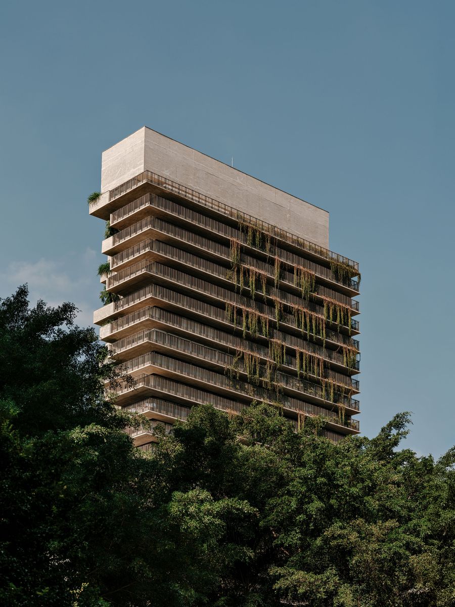 The Ibaté building dramatically rises above a canopy of lush green trees, showcasing its striking brutalist facade intertwined with cascading vegetation. The concrete and integrated plants create a unique dialogue between urban density and natural softness, characteristic of Studio Arthur Casas's design. The Ibaté building dramatically rises above a canopy of lush green trees, showcasing its striking brutalist facade intertwined with cascading vegetation. The concrete and integrated plants create a unique dialogue between urban density and natural softness, characteristic of Studio Arthur Casas's design.