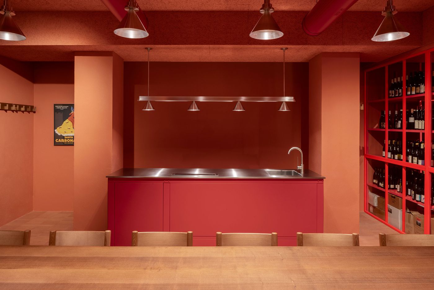 A bold, monochromatic scene at Santo Palato by Naessi Studio, featuring a vibrant red bar counter with a stainless steel sink, set against terracotta-hued walls and ceiling. Industrial pendant lights illuminate the space. A striking red metal shelving unit brimming with wine bottles adds a dramatic vertical element, reflecting a modern industrial aesthetic. A bold, monochromatic scene at Santo Palato by Naessi Studio, featuring a vibrant red bar counter with a stainless steel sink, set against terracotta-hued walls and ceiling. Industrial pendant lights illuminate the space. A striking red metal shelving unit brimming with wine bottles adds a dramatic vertical element, reflecting a modern industrial aesthetic.
