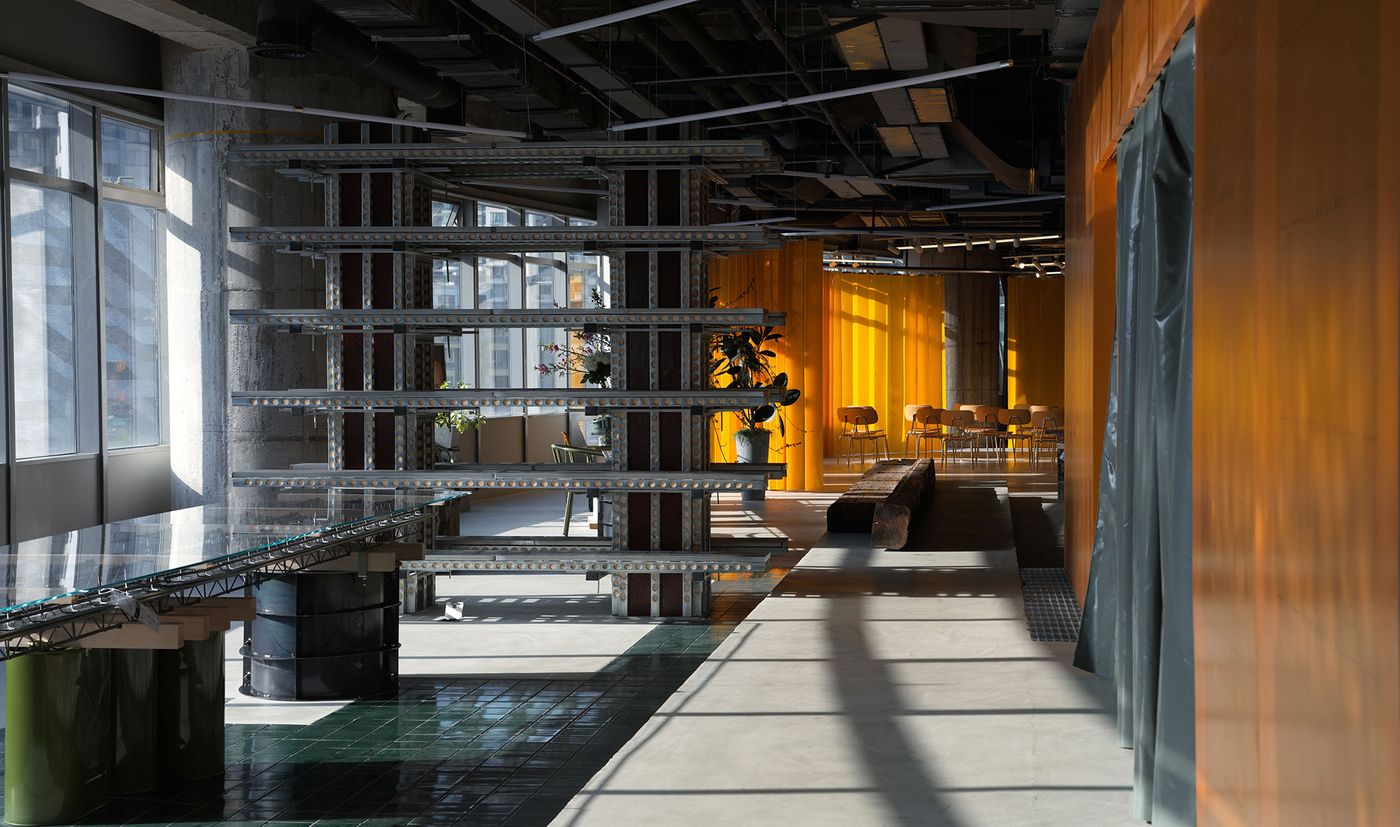 Sunlight streams into 889 GLO Art Space, illuminating a pathway between a robust industrial shelving unit and a long wooden bench. The vibrant yellow partition walls create a vivid backdrop, contrasting with the raw concrete and dark ceiling, while a unique dark green tiled floor adds texture, showcasing a bold industrial design with playful color accents. Sunlight streams into 889 GLO Art Space, illuminating a pathway between a robust industrial shelving unit and a long wooden bench. The vibrant yellow partition walls create a vivid backdrop, contrasting with the raw concrete and dark ceiling, while a unique dark green tiled floor adds texture, showcasing a bold industrial design with playful color accents.