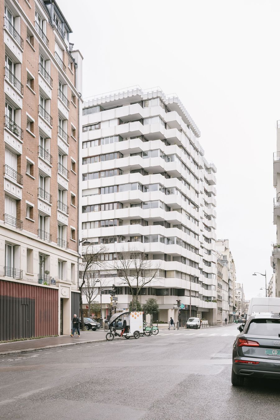 Urban street scene featuring modern white apartment buildings, a parked car, and people walking, under a cloudy sky. Urban street scene featuring modern white apartment buildings, a parked car, and people walking, under a cloudy sky.