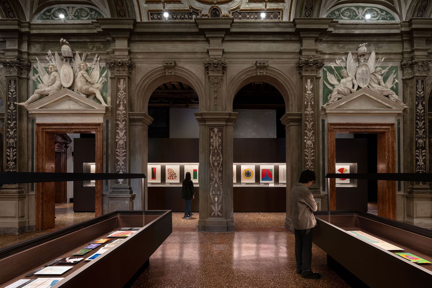 Interior of a gallery showcasing colorful artworks in illuminated displays, framed by ornate architecture and classical sculptures. Interior of a gallery showcasing colorful artworks in illuminated displays, framed by ornate architecture and classical sculptures.